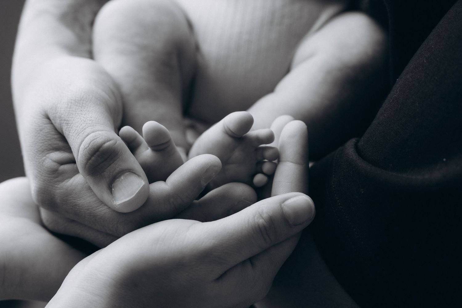 Close-up black and white images focusing on gentle hands holding a baby.
