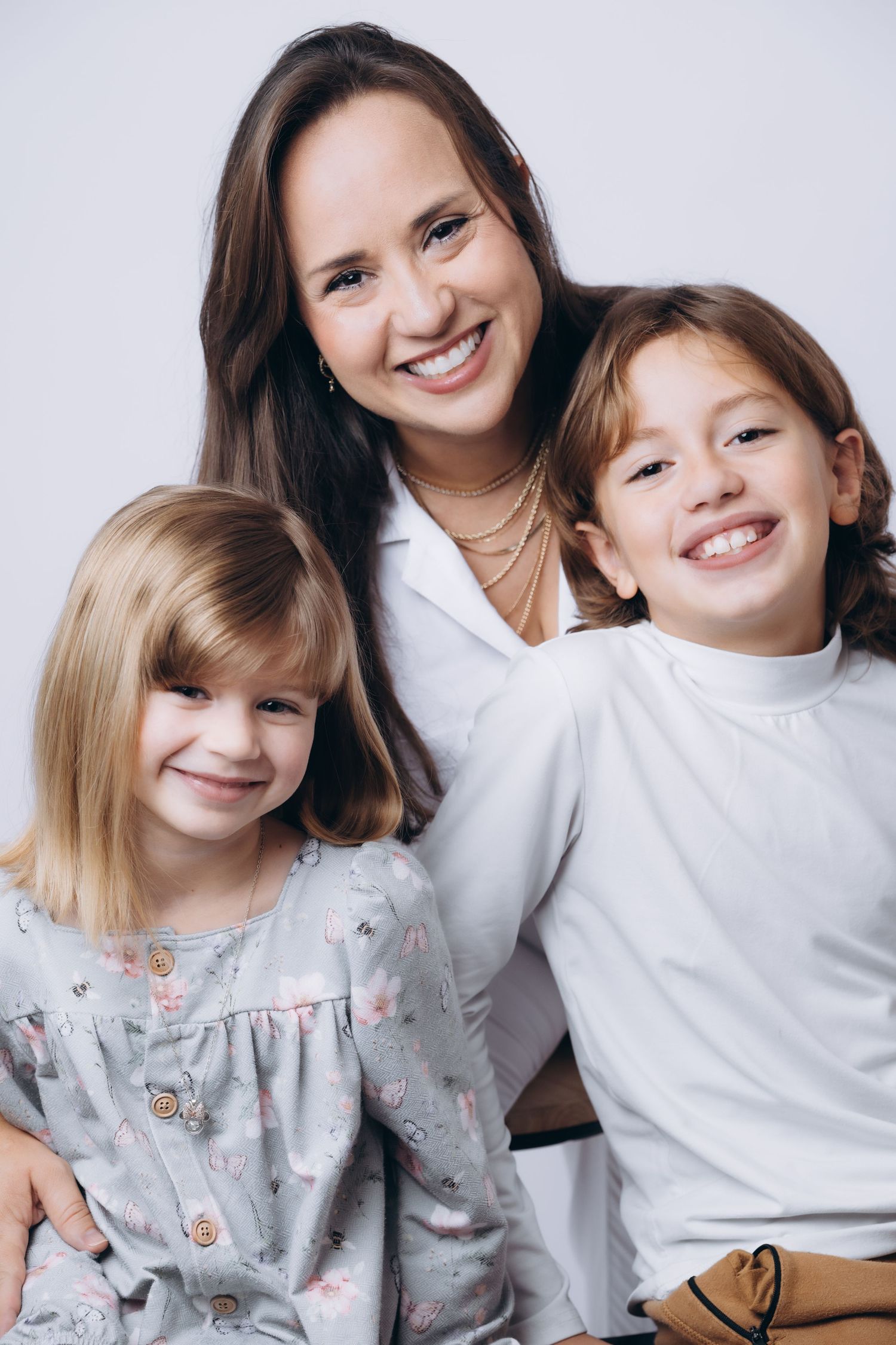 Portrait of three people in coordinated outfits sharing bright smiles against white background.