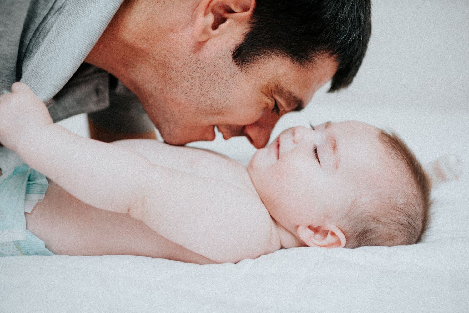 Intimate bonding moment between parent and infant on white bedding.