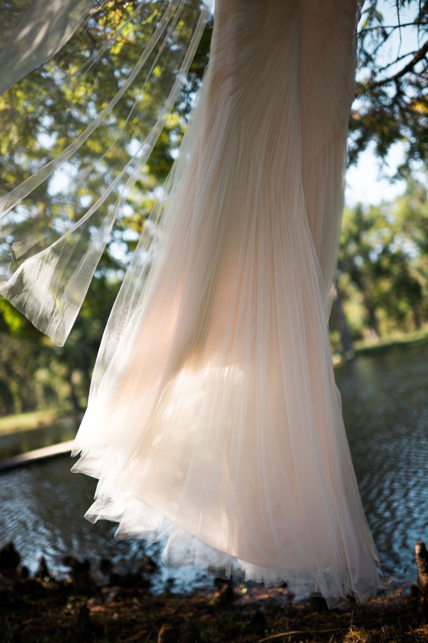 Ethereal wedding dress skirt flowing in soft sunlight by a lake.