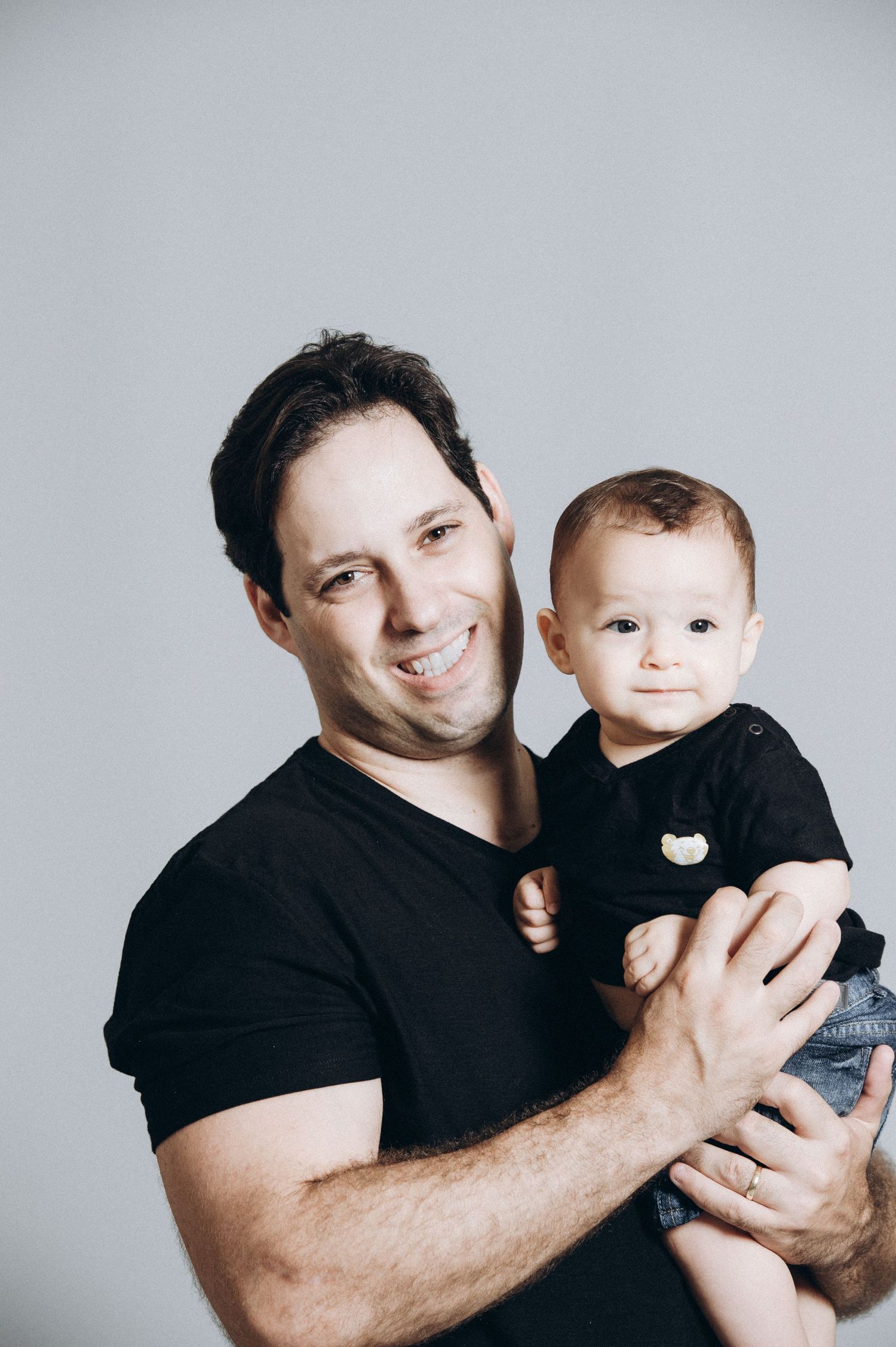 Studio portraits of a parent and baby in matching black outfits against a gray background.