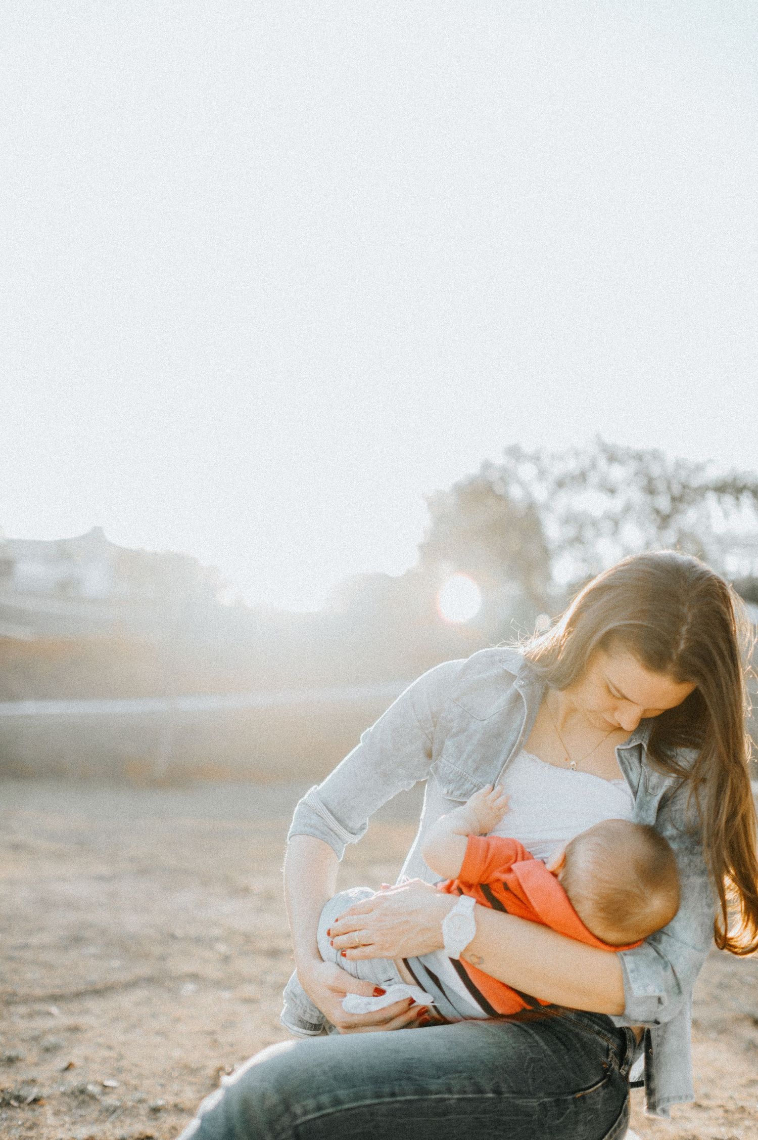 Parent and infant cuddle together during golden hour outdoor photoshoot.