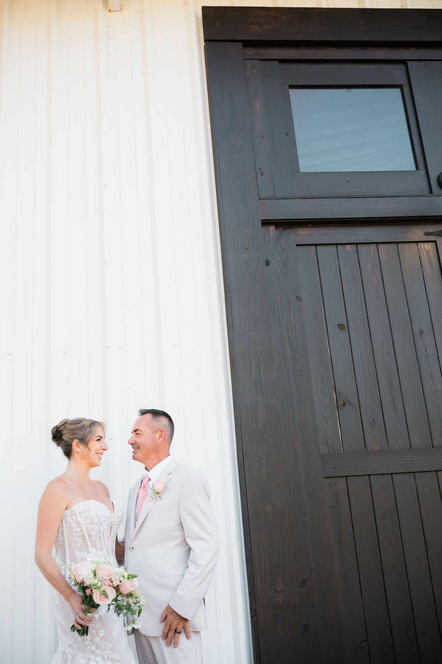 Newlyweds share intimate moment against white wall and dark doors.