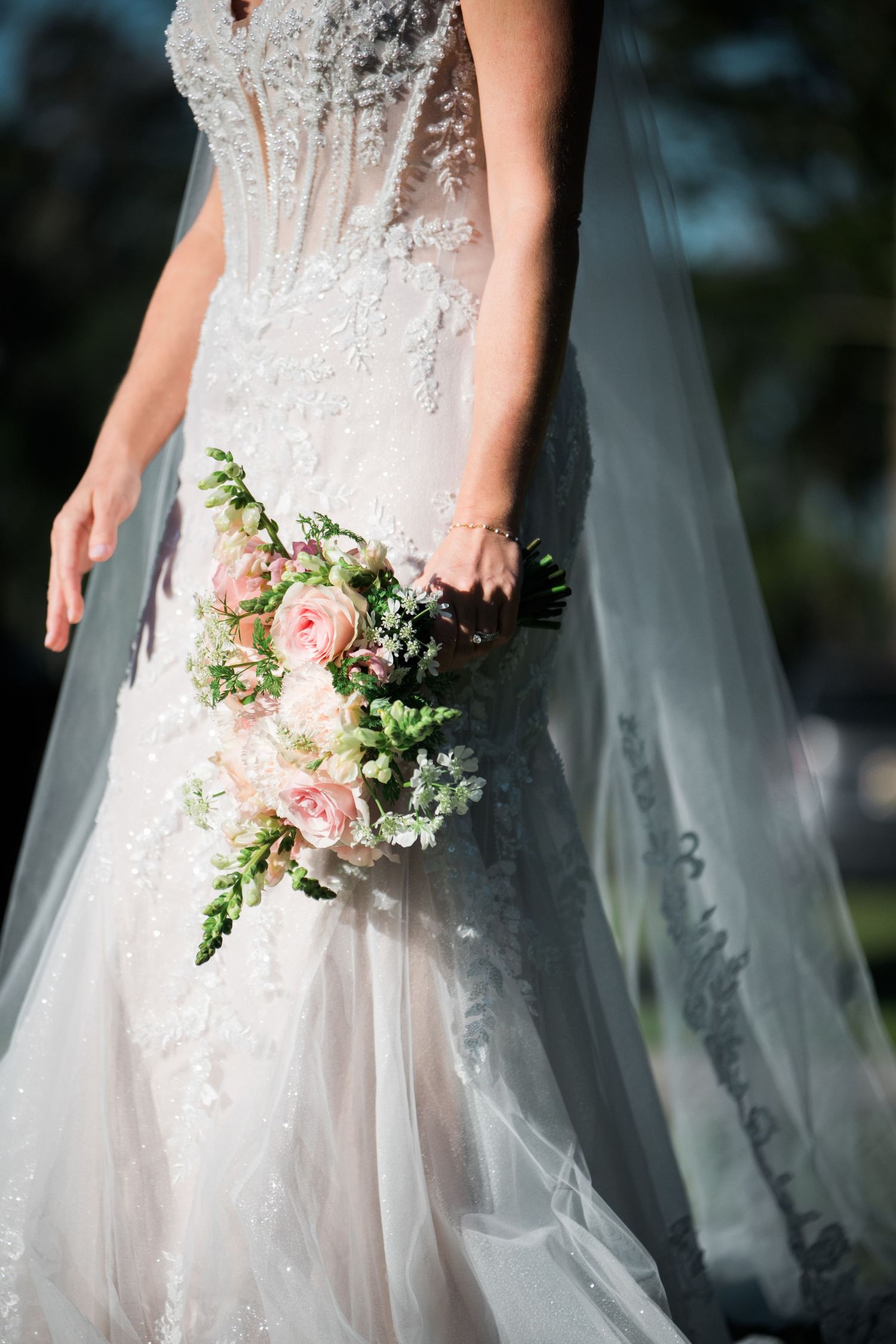 Close-up of a white wedding dress with delicate lace details and pink floral bouquet.