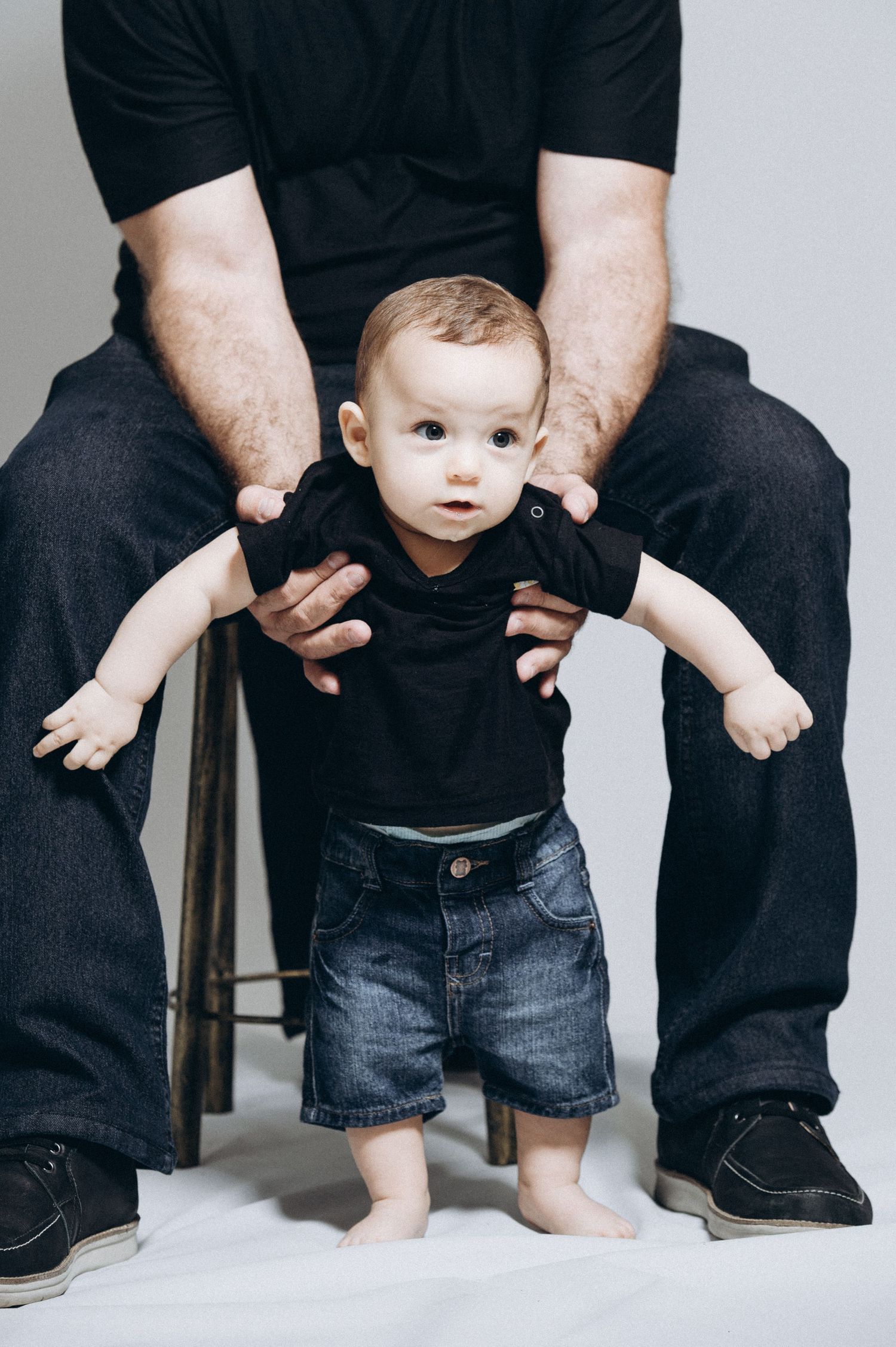 Close-up of baby feet and legs next to adult wearing dark clothing on a white background.