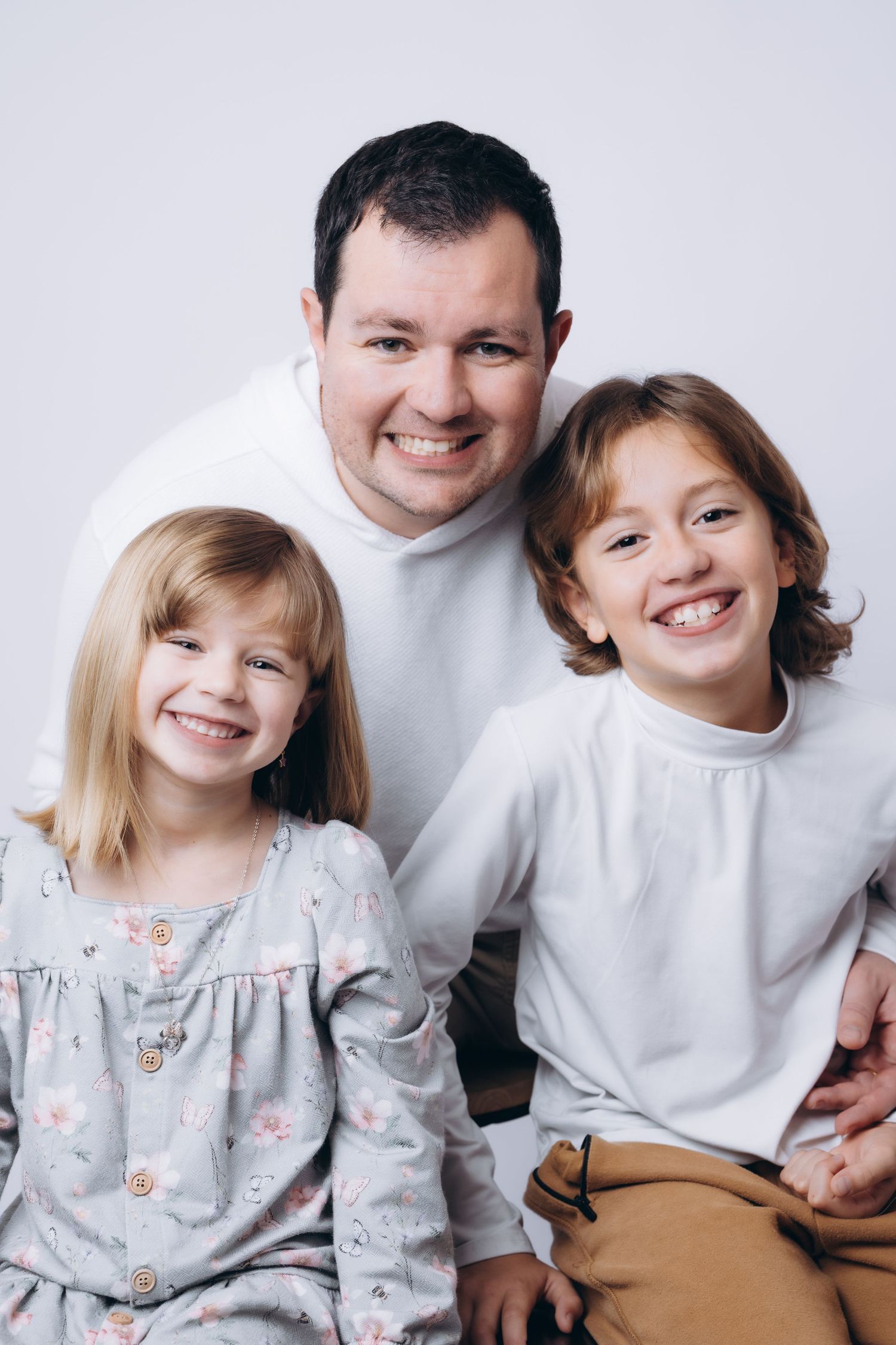 Family portrait showing three people in white and casual attire smiling warmly at camera.