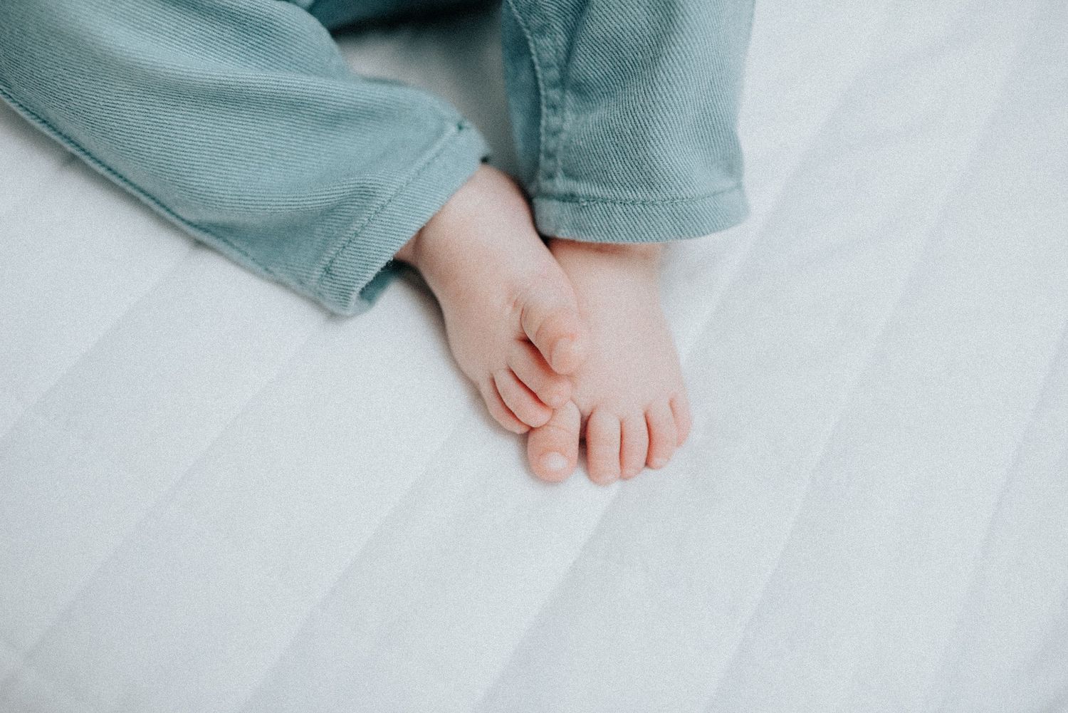 Baby's feet and legs rest on white floor during lifestyle photoshoot.