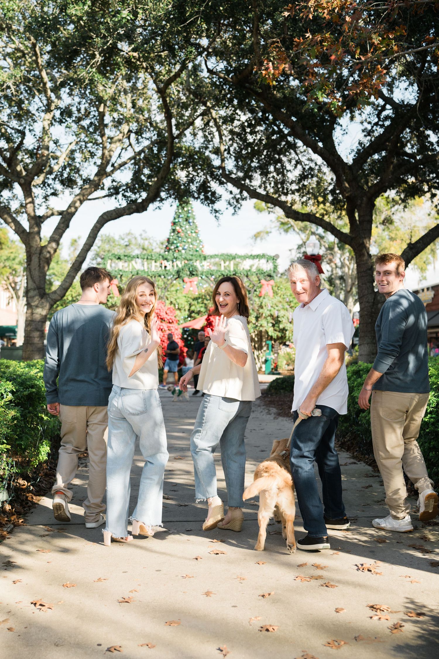 A group interacts casually during an outdoor photoshoot beneath trees on a sunny day.