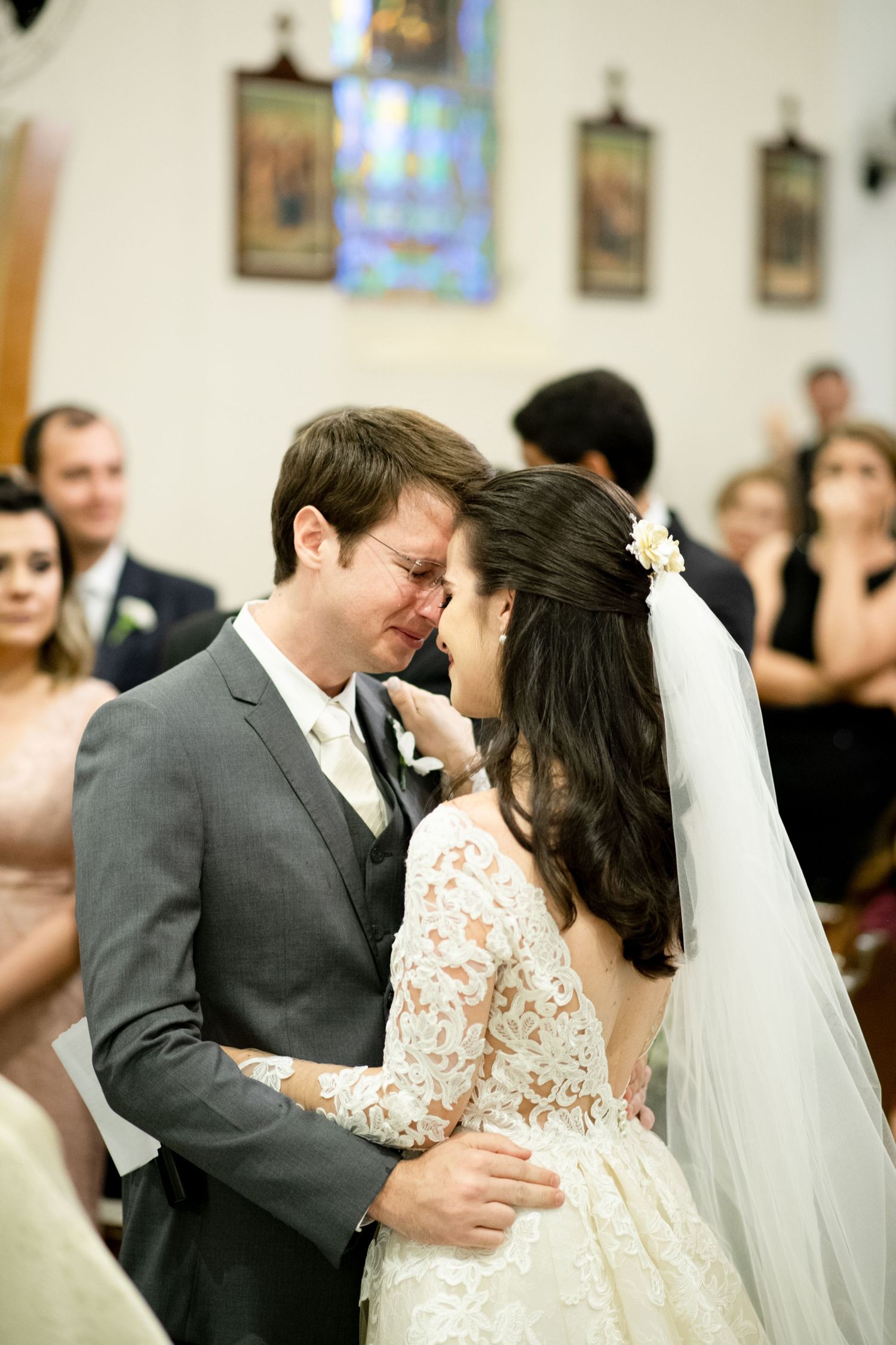 Intimate moment between couple during church wedding ceremony with stained glass background.