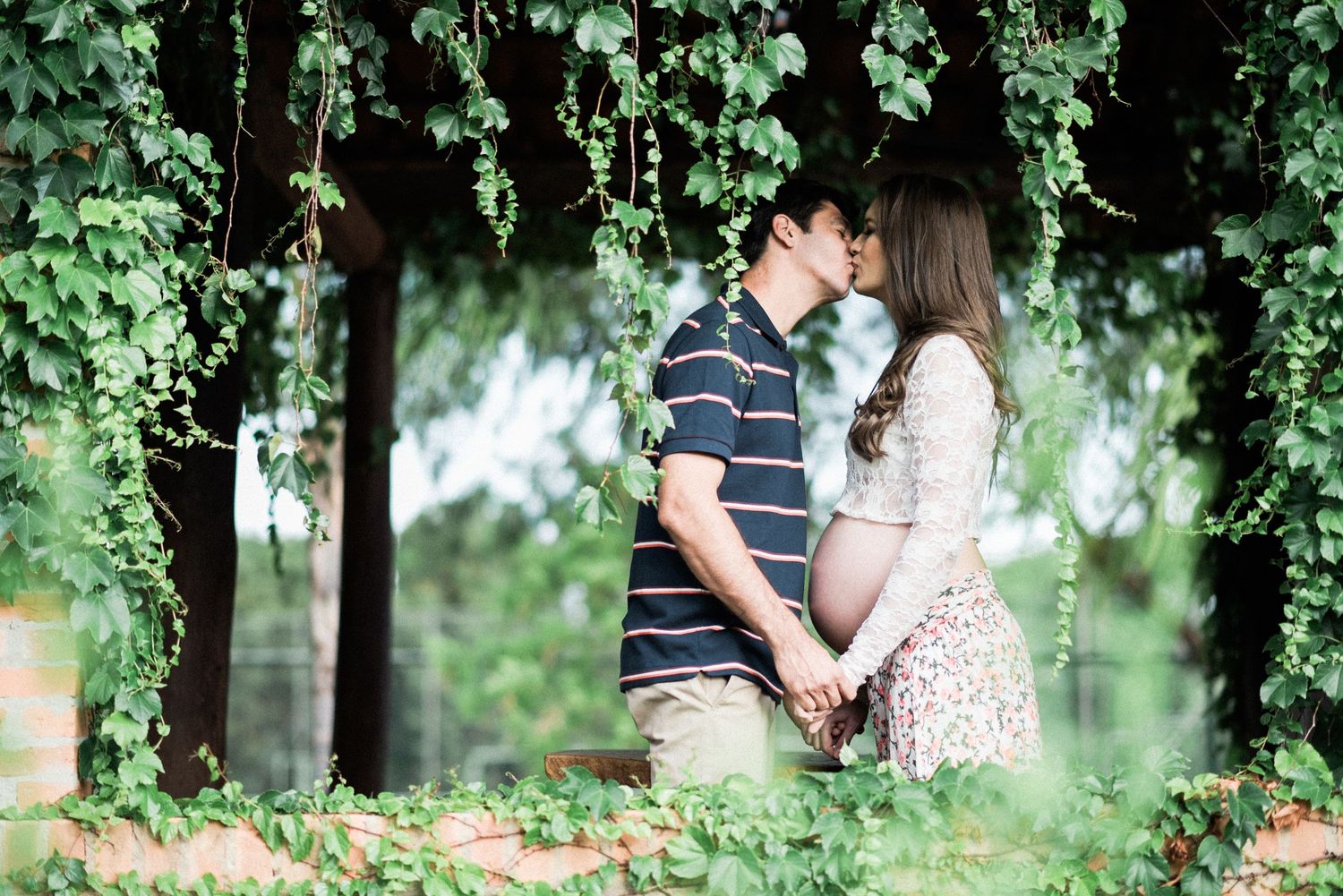 Couple embracing under green foliage in a romantic outdoor photoshoot.