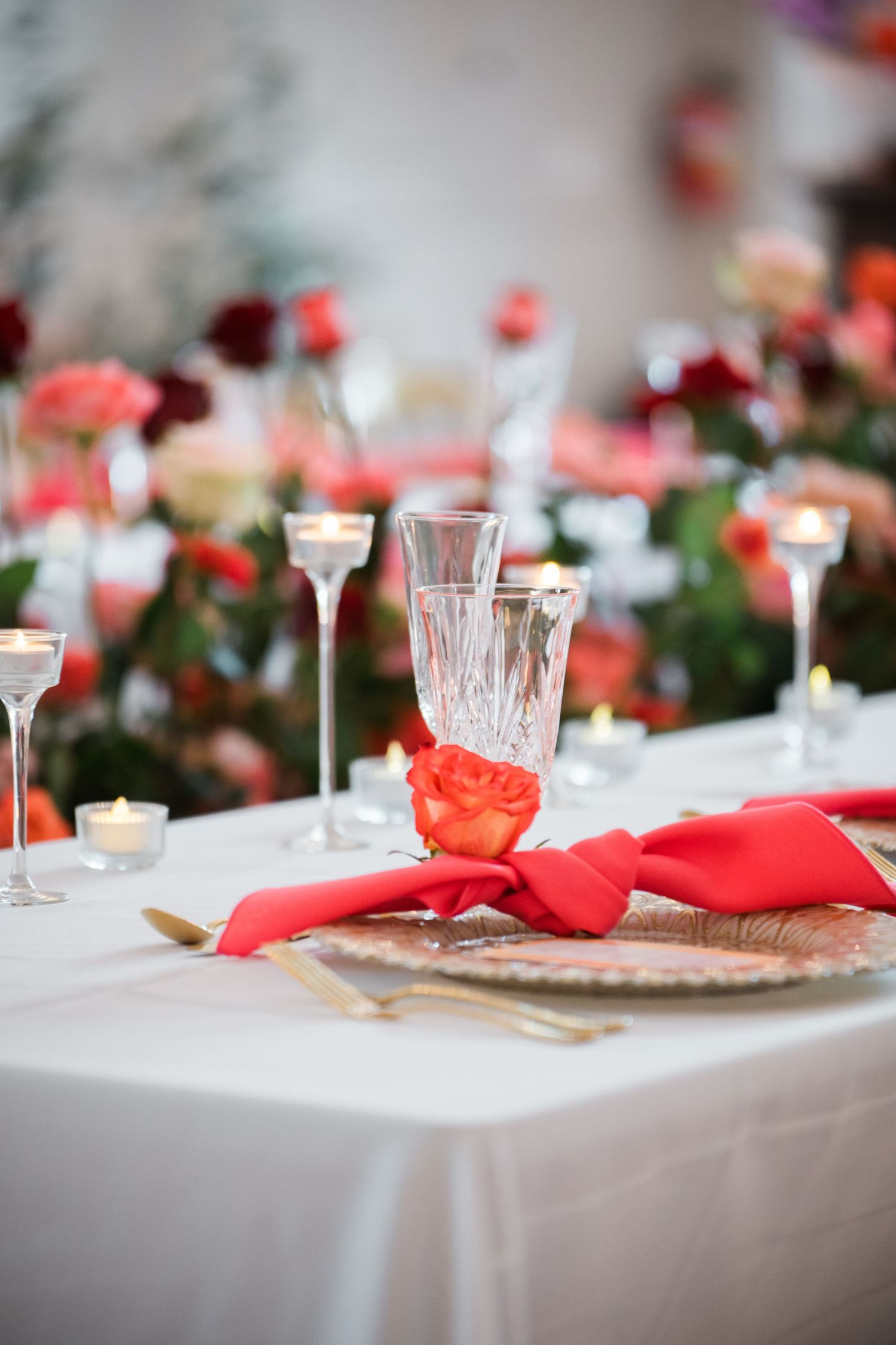 Elegant table setting with red floral accents, crystal glasses, and white linens.