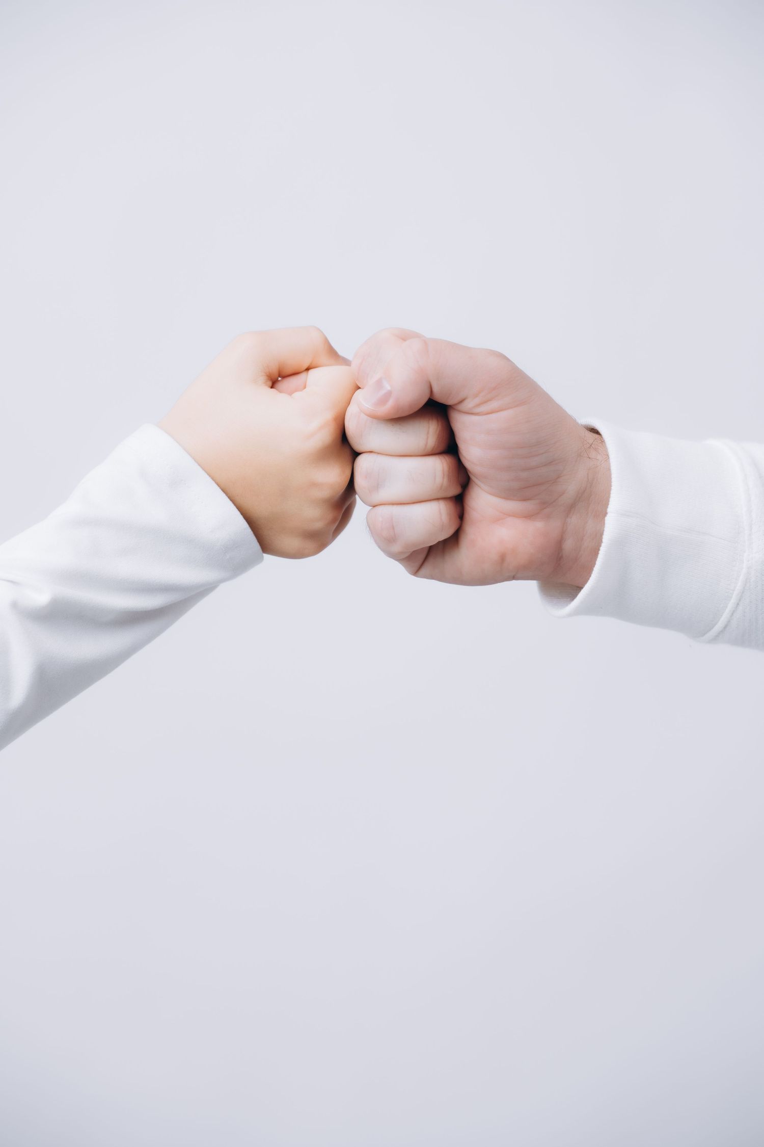 Close-up of two fists bumping together wearing white long sleeves against light background.