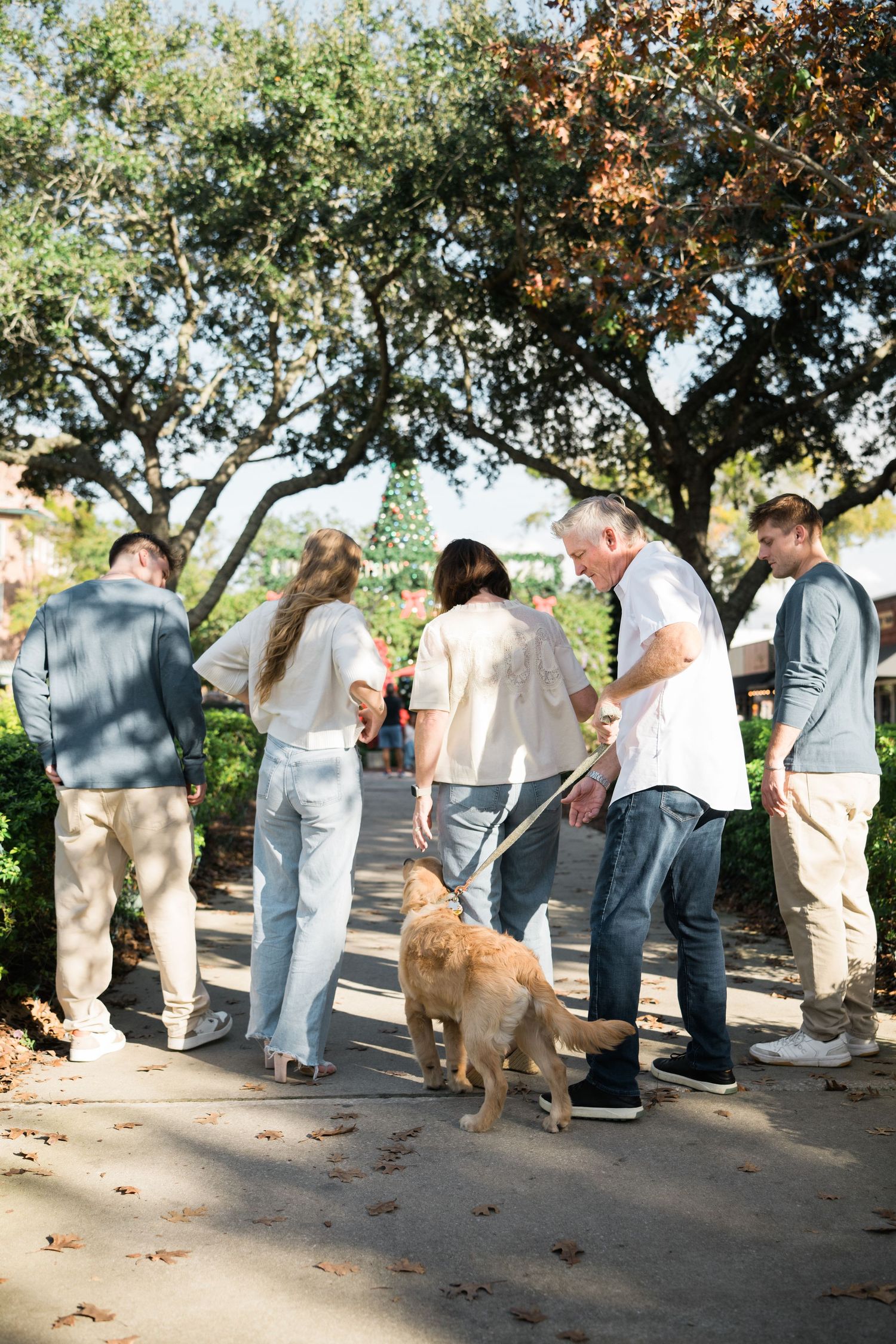 People and a golden retriever dog gather for casual outdoor photos under trees.