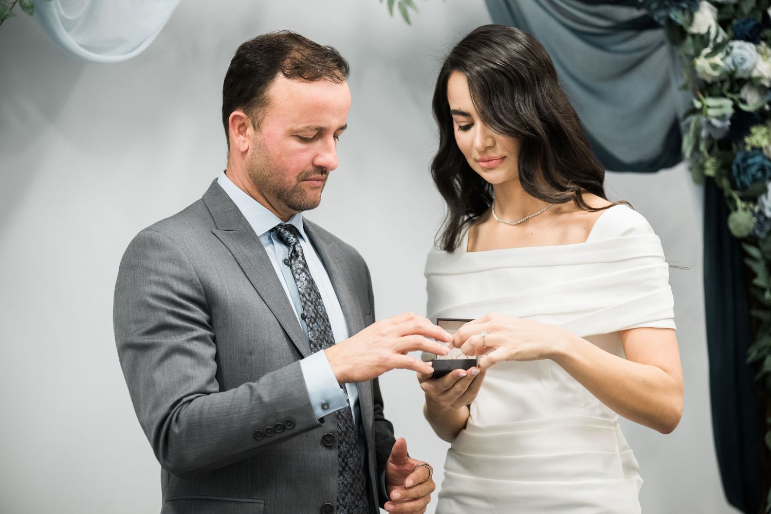 A couple exchanges rings during an intimate ceremony with floral decorations.