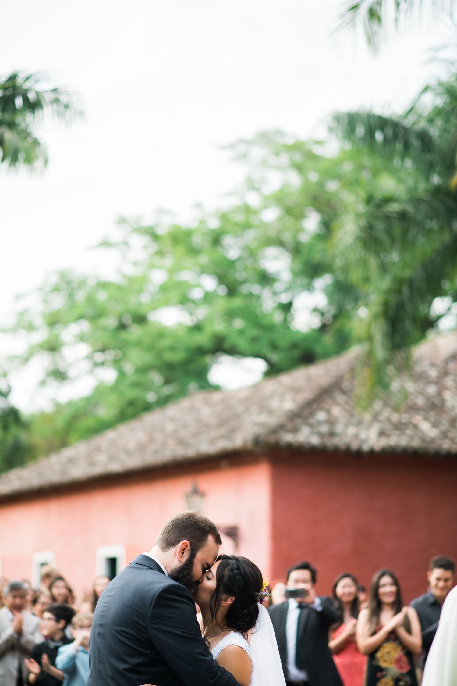 Wedding guests watch as the ceremony unfolds in front of a coral-colored building with palm trees.