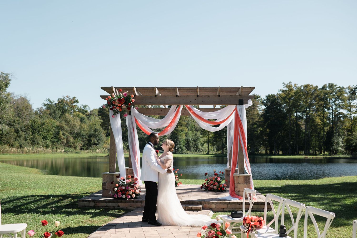 Wedding ceremony venue with white chairs and floral decorations beside a serene lake.