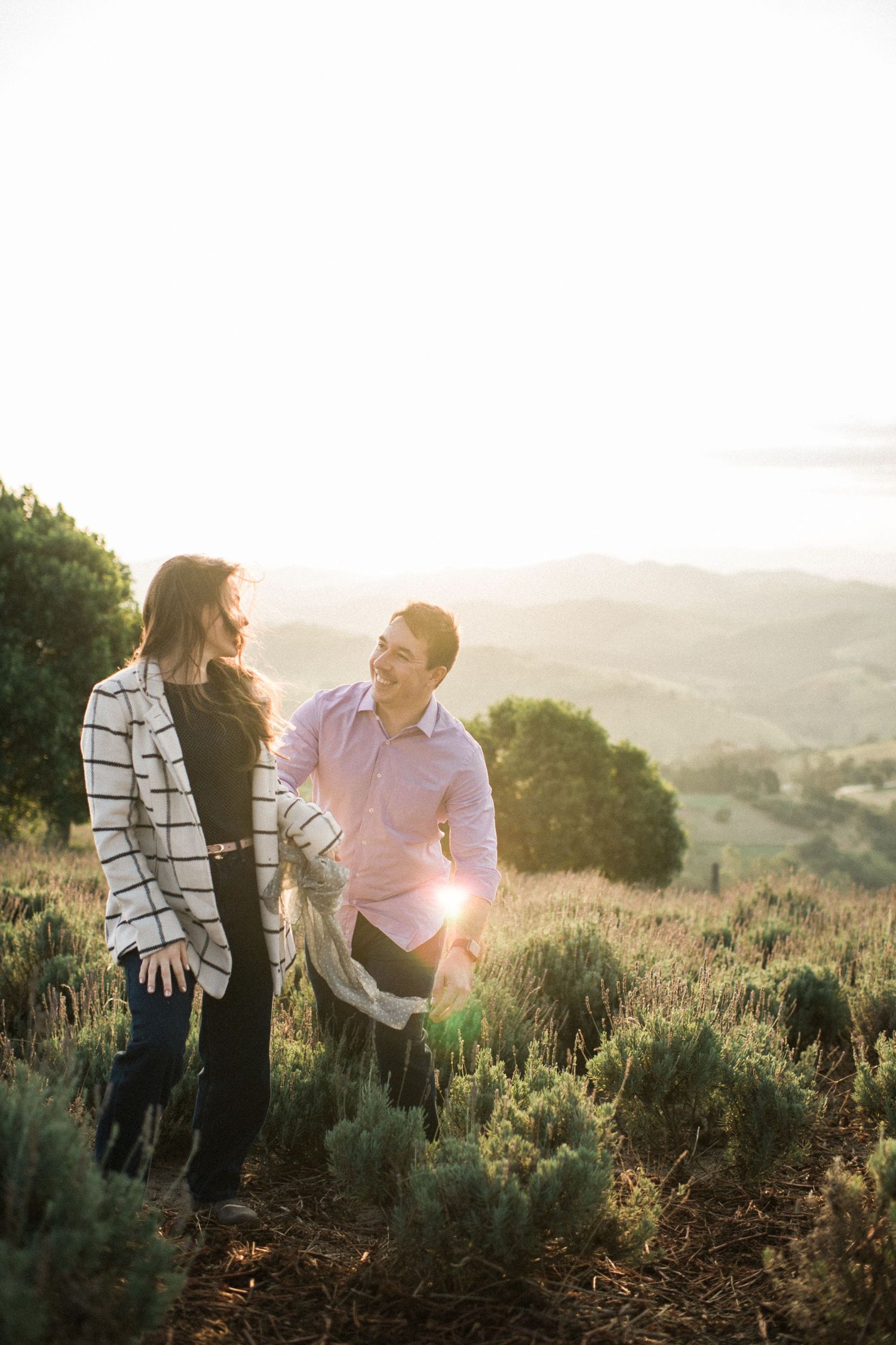 Romantic couple embraces during golden hour sunset in a scenic hillside meadow.