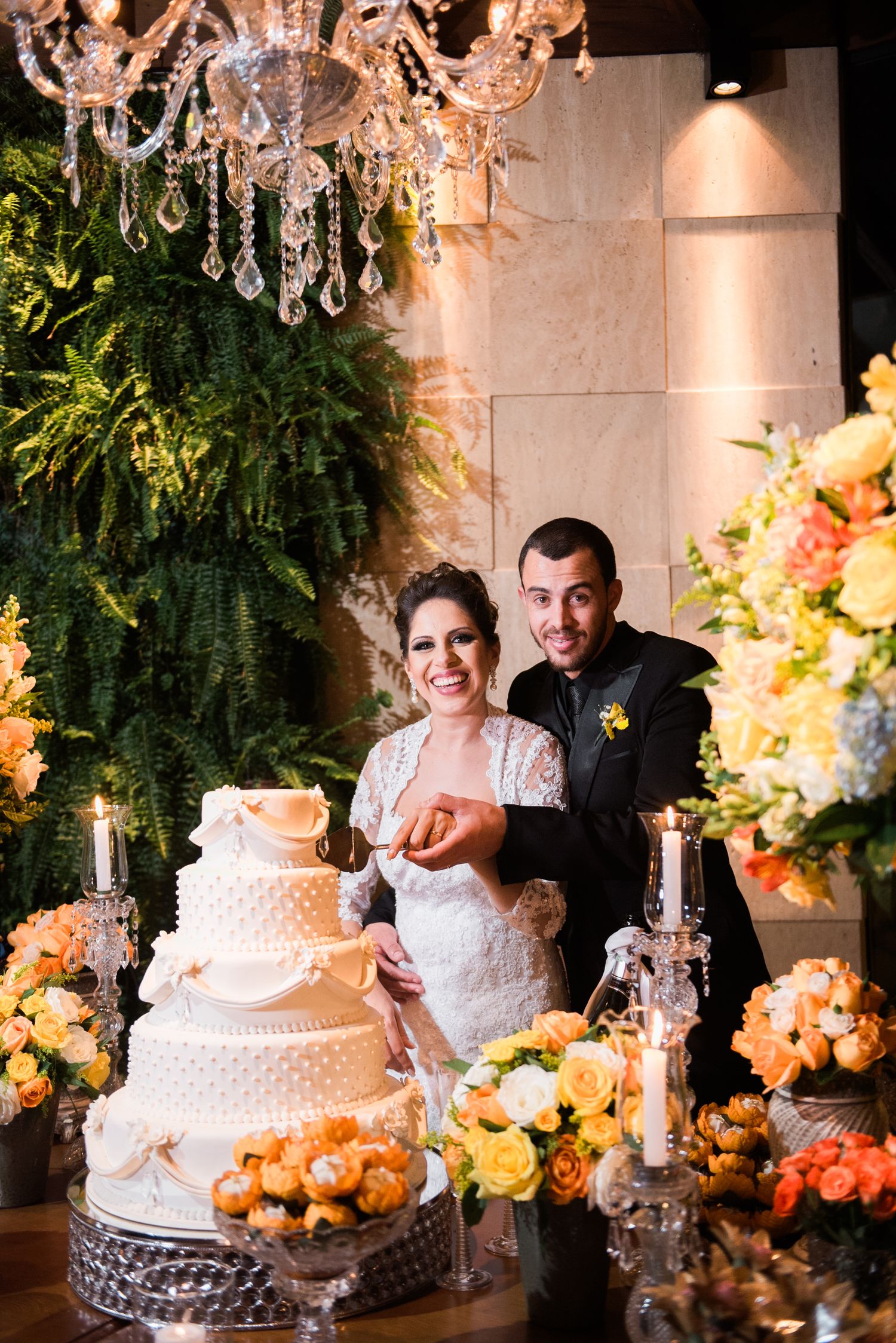 Elegant wedding reception setup with crystal chandeliers and floral decorations around tiered cake.
