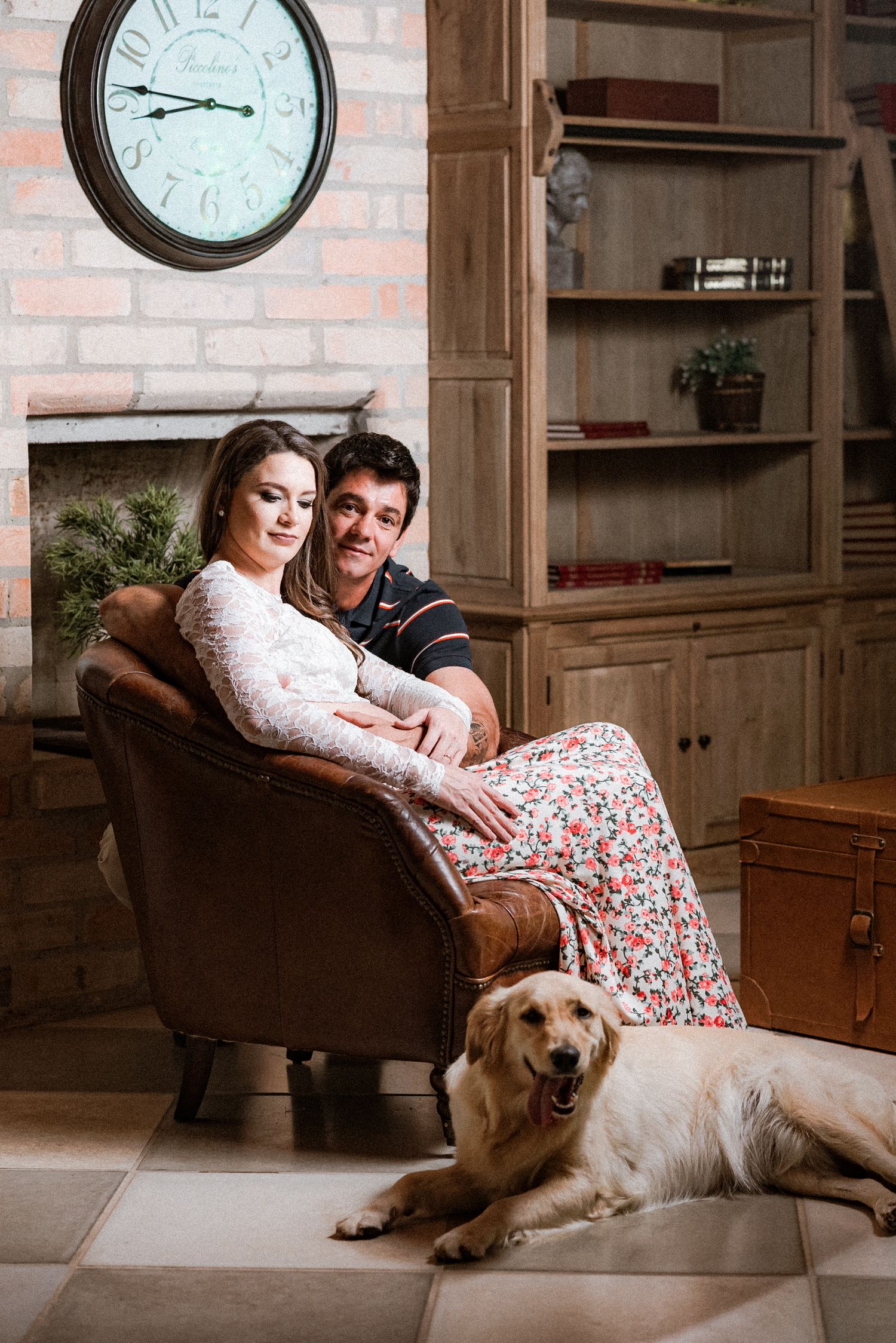 Couple relaxes on leather couch with their golden retriever in cozy brick-walled room.