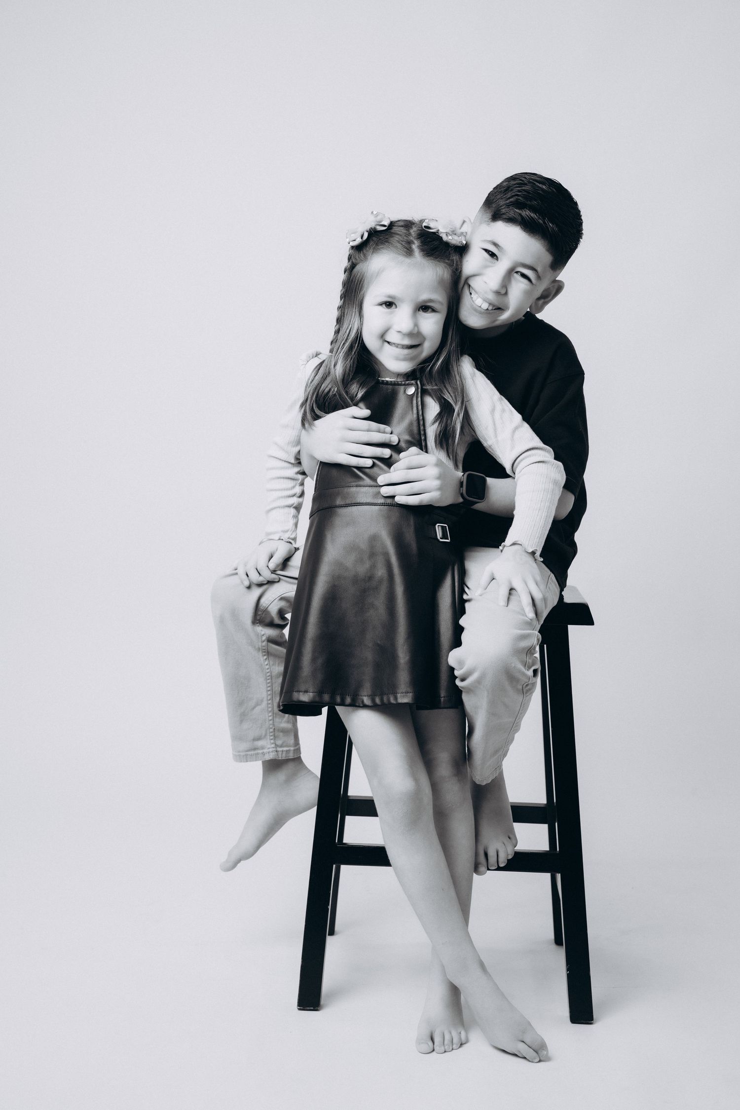 Artistic black and white photos of siblings sitting together on a wooden stool.