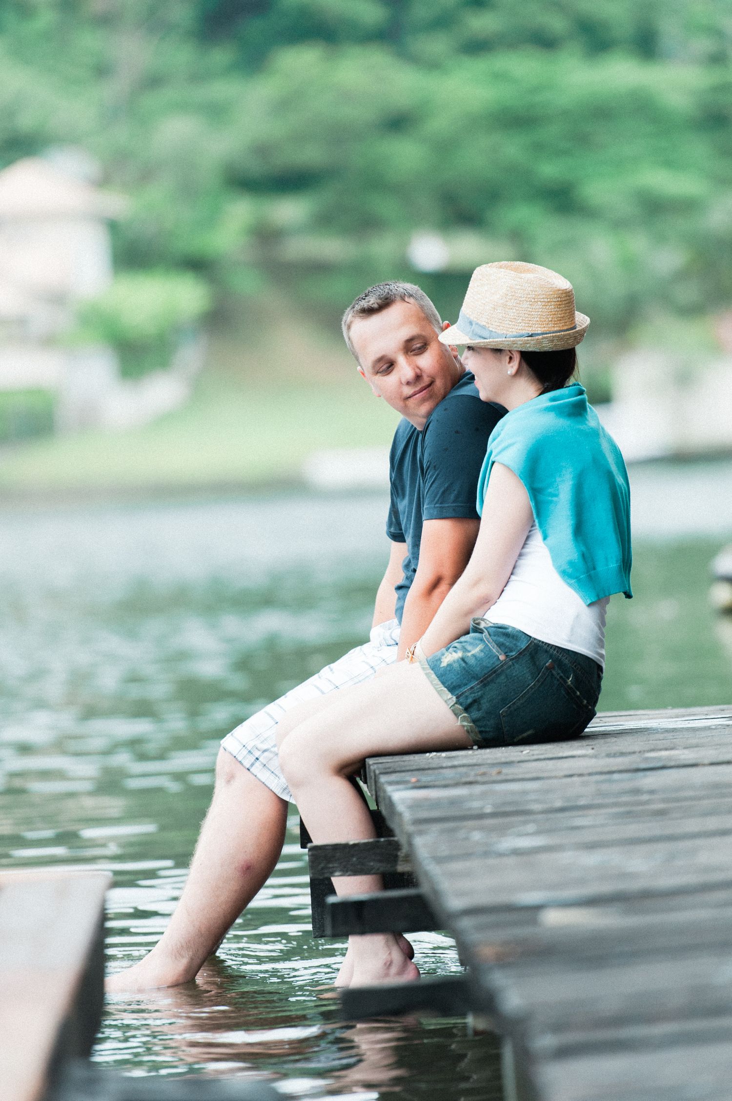 People dipping their feet in lake water while sitting on a rustic wooden dock.