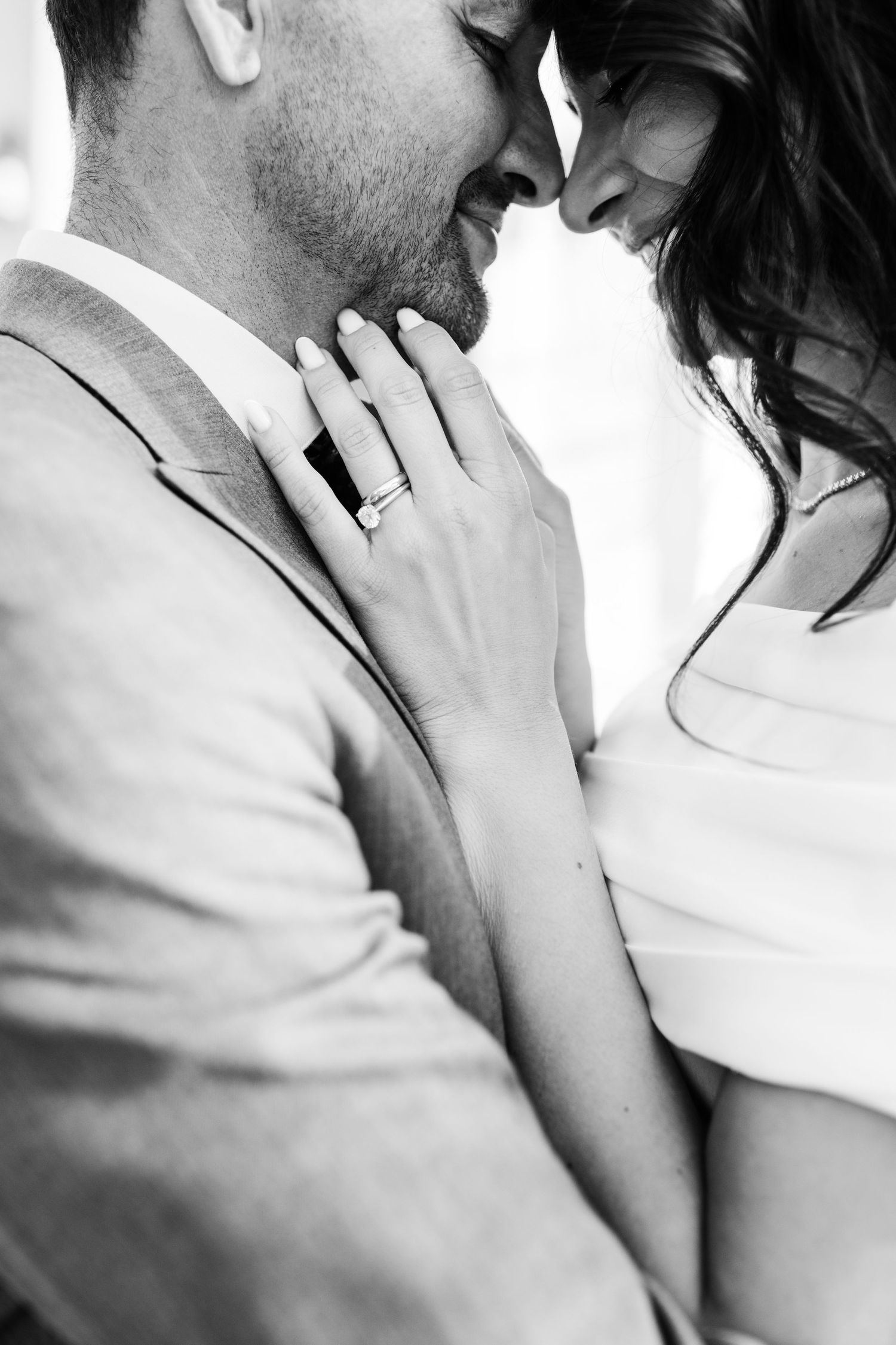 Close-up black and white photo of a couple in an intimate embrace showing an engagement ring.