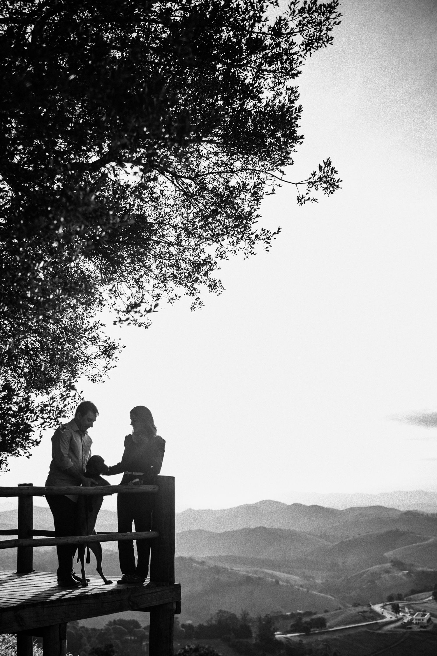 Silhouettes of people sitting on a bench overlooking mountain vistas in black and white.