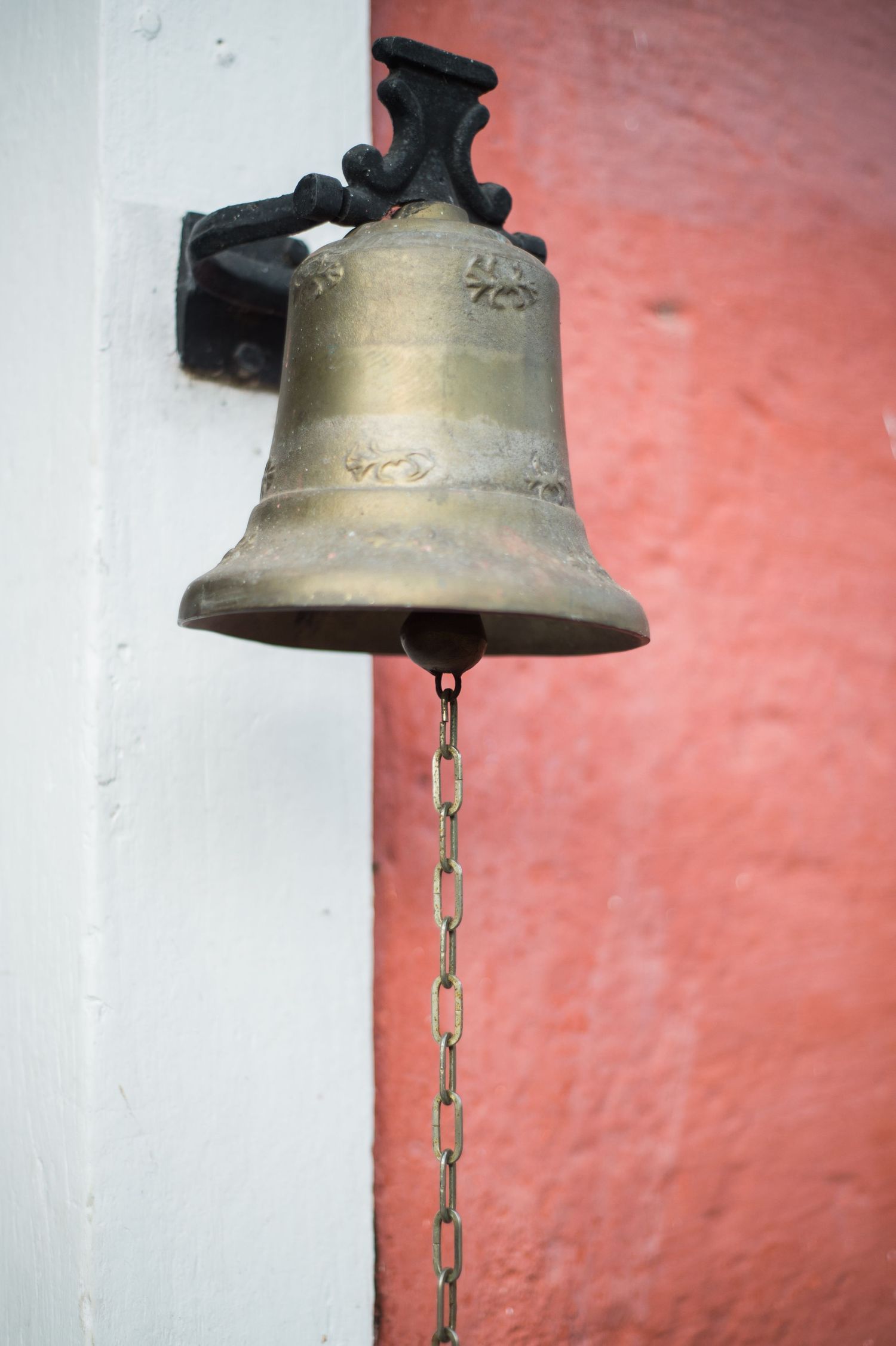 Vintage brass bell mounted on coral-colored wall with hanging chain.
