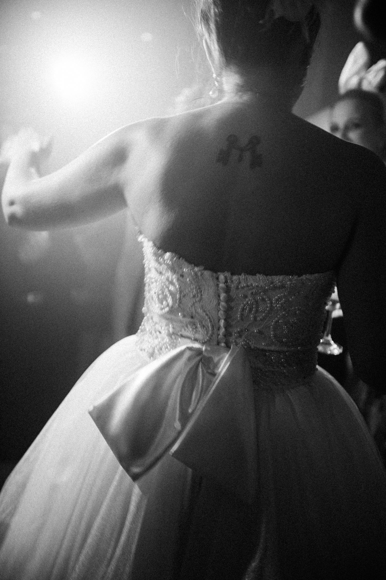 Black and white photo of a bride in a lace corset wedding dress with a small tattoo visible on her back.