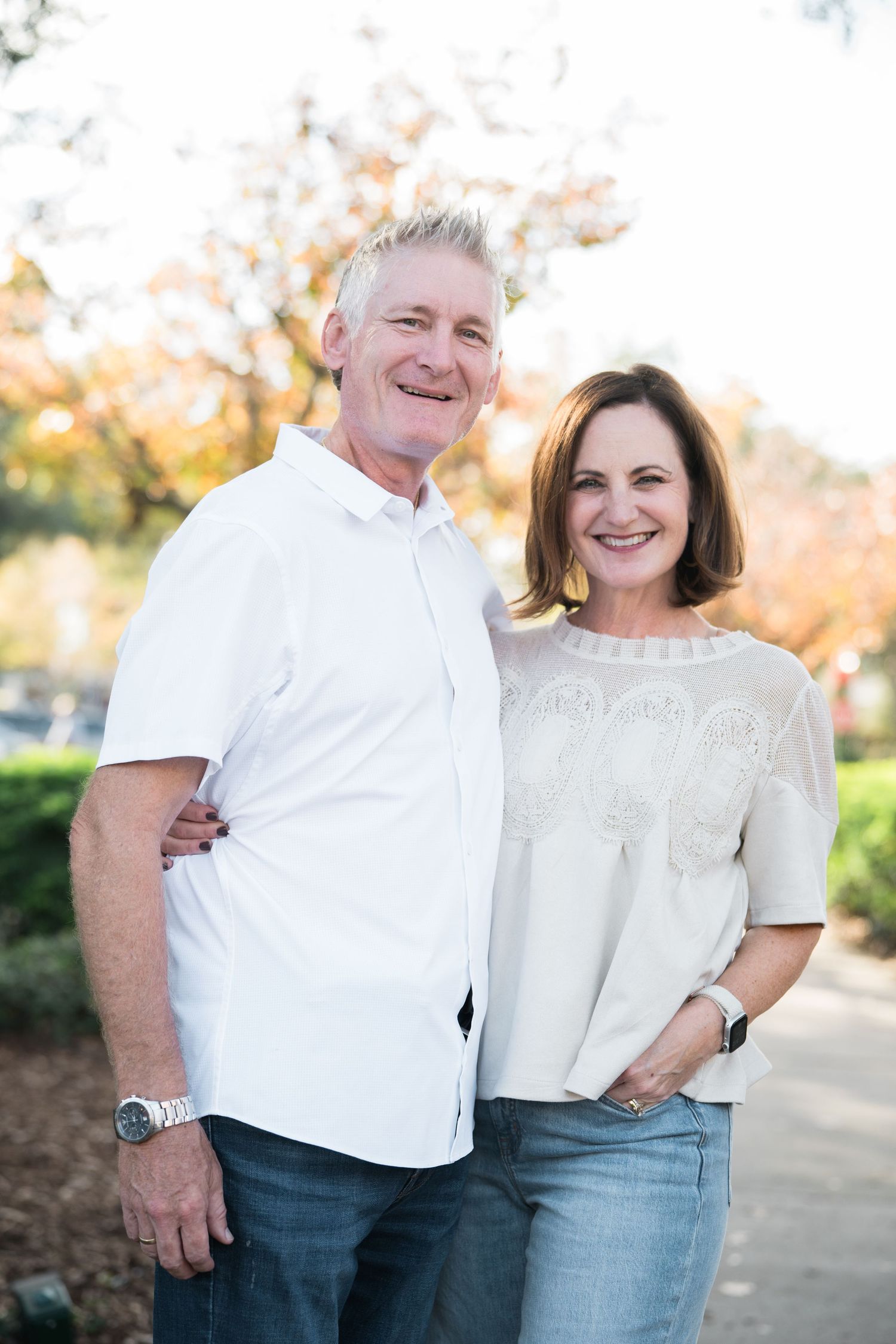 Couple in matching white tops and jeans pose together outdoors during autumn.