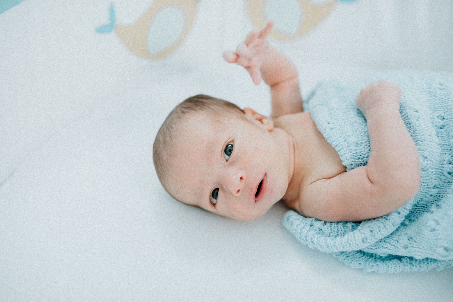 Newborn baby in light blue outfit lying on white backdrop.