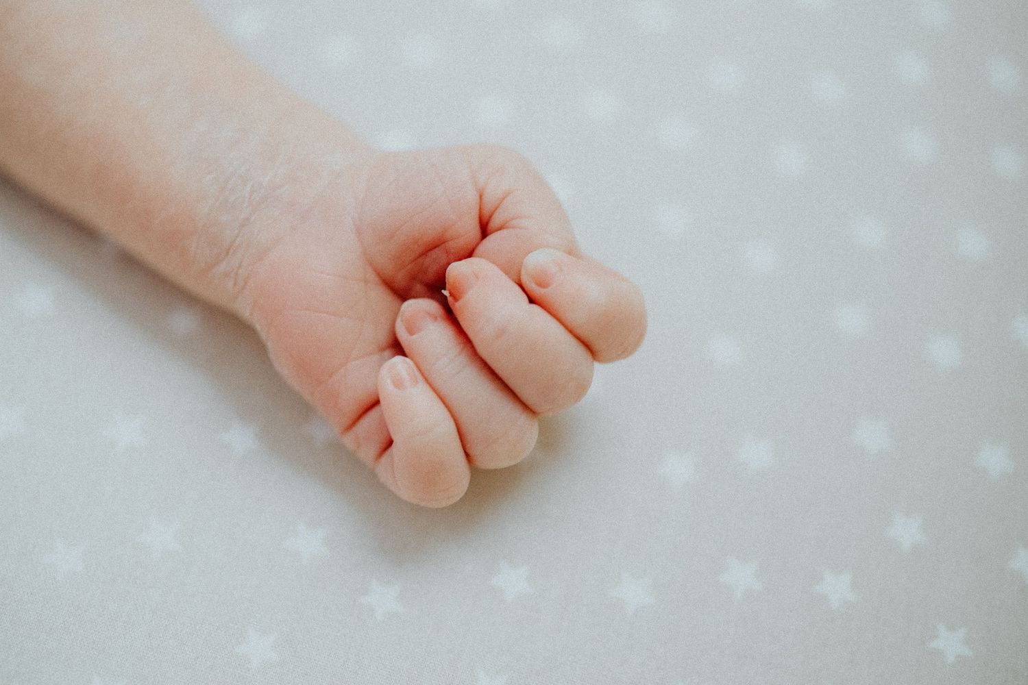 Detail shots of tiny baby fingers and hands on dotted white fabric.