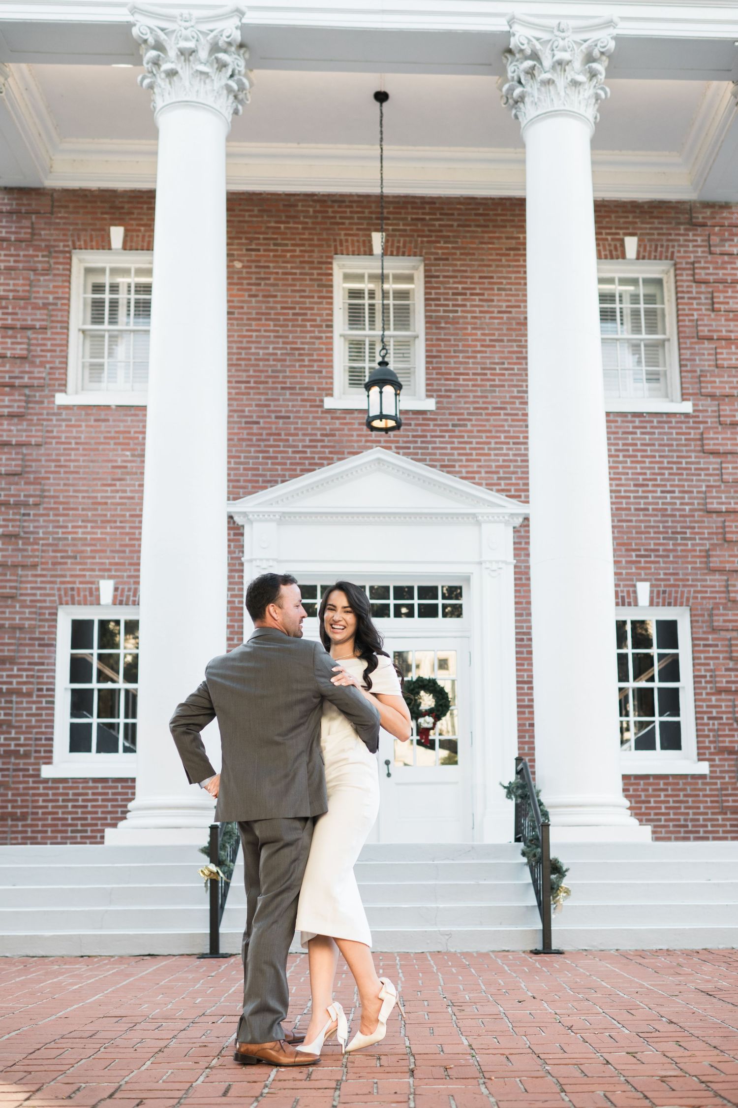 A couple poses in front of a grand colonial building with white columns and brick facade.