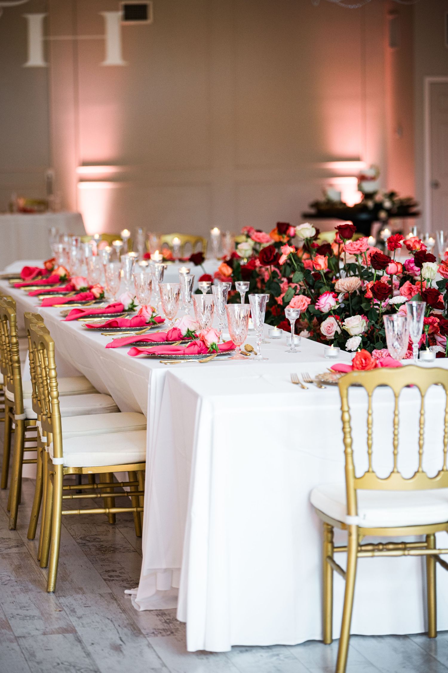 Elegant wedding reception table with pink floral centerpieces, gold chairs, and white linens.