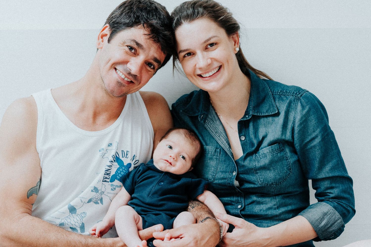 Family portrait with baby in casual setting against light wall.
