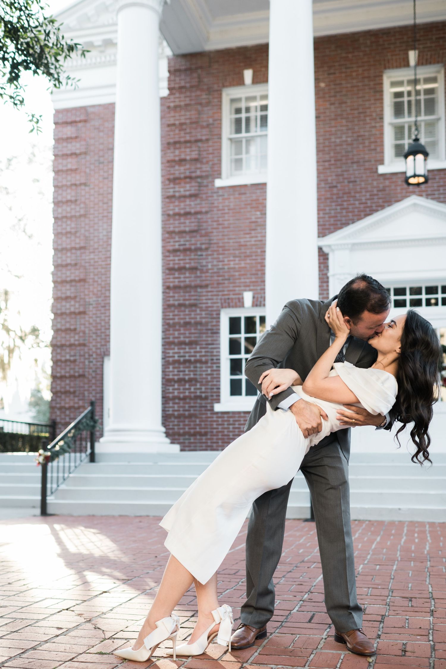 A dramatic dip pose in front of a classic brick building with white columns.