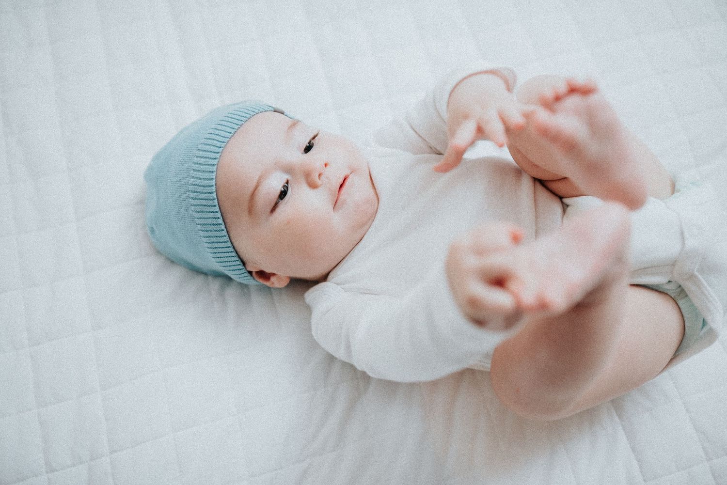 Infant in blue cap and white clothing rests peacefully.