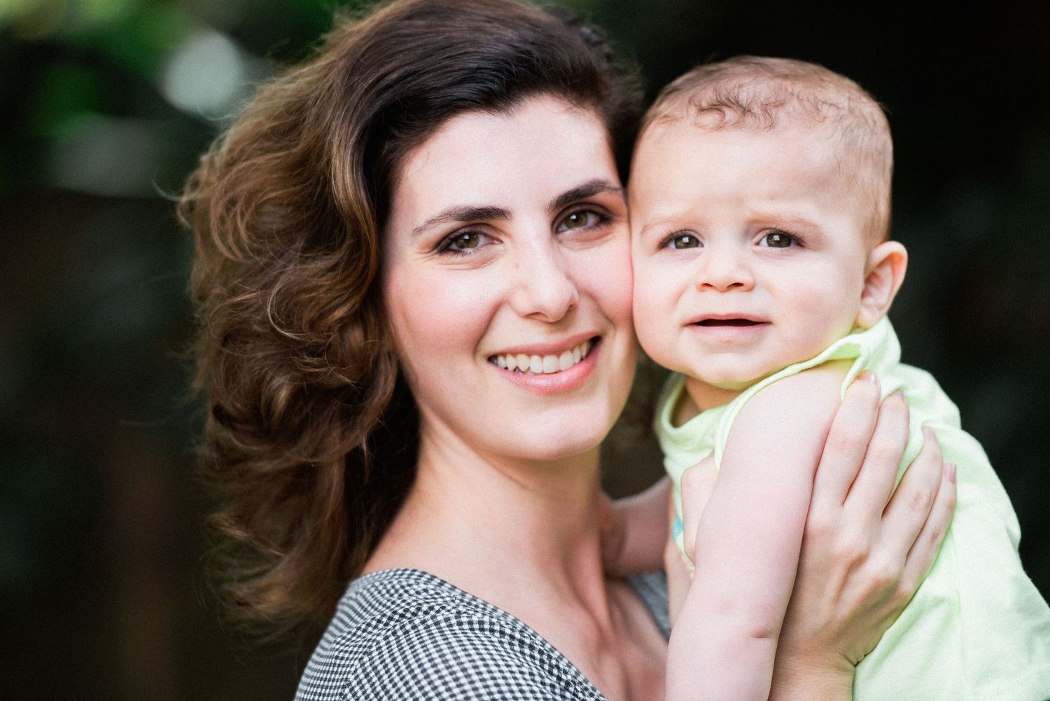 Sweet candid moment between adult and baby against blurred outdoor background.