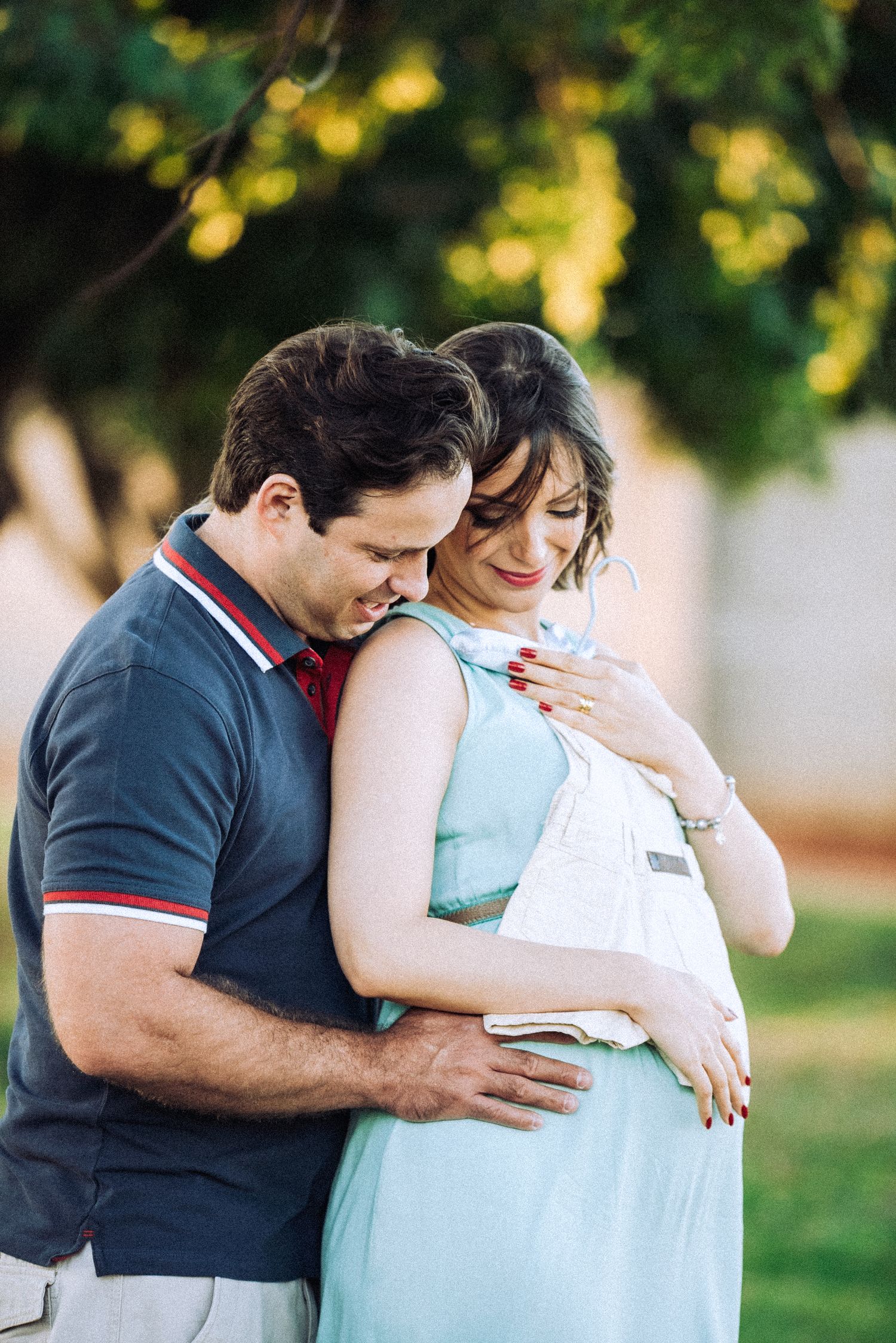 Intimate moment between couple during maternity photo session in park setting.