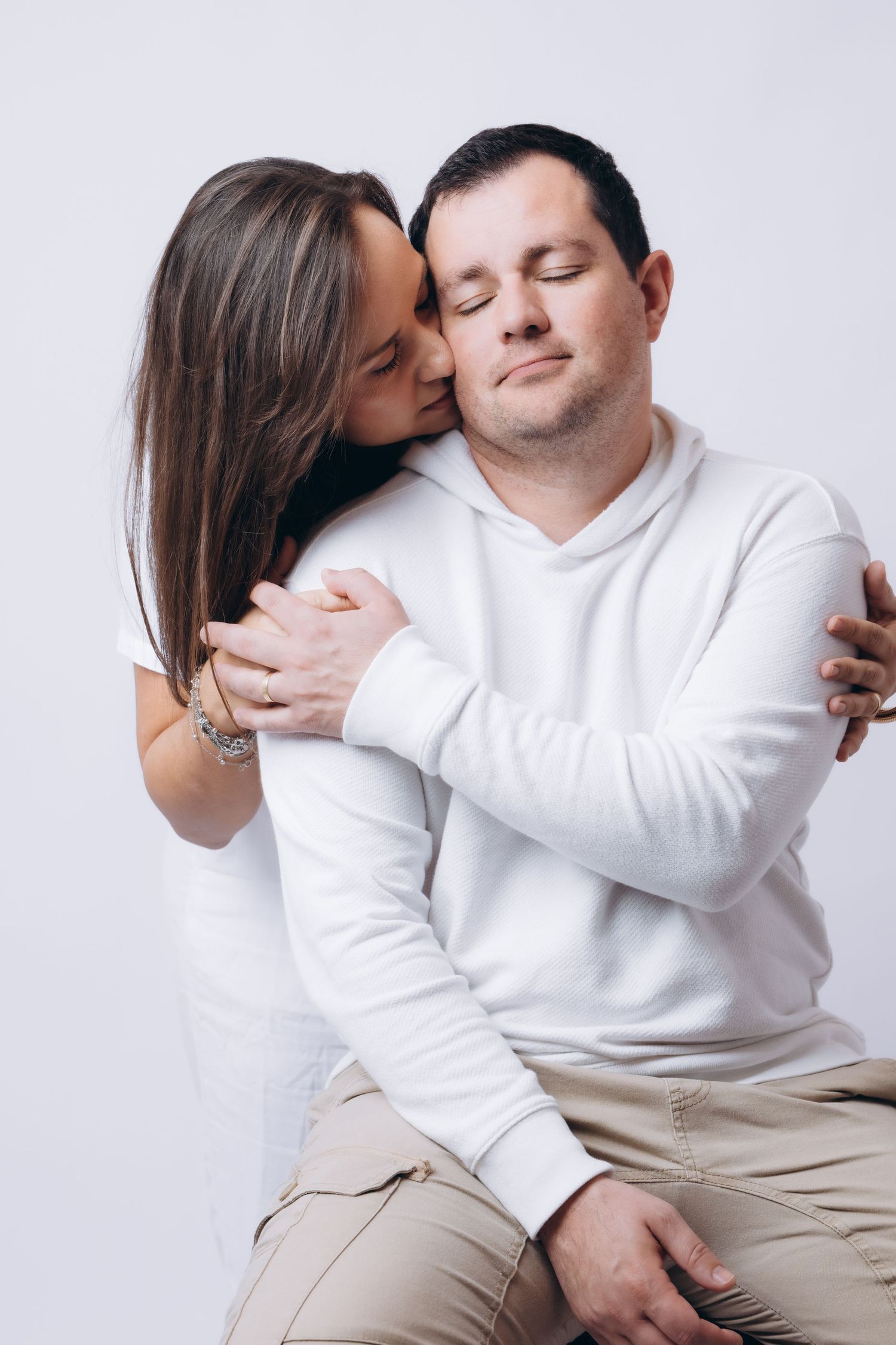 Intimate moment between couple in white as they embrace against light background.
