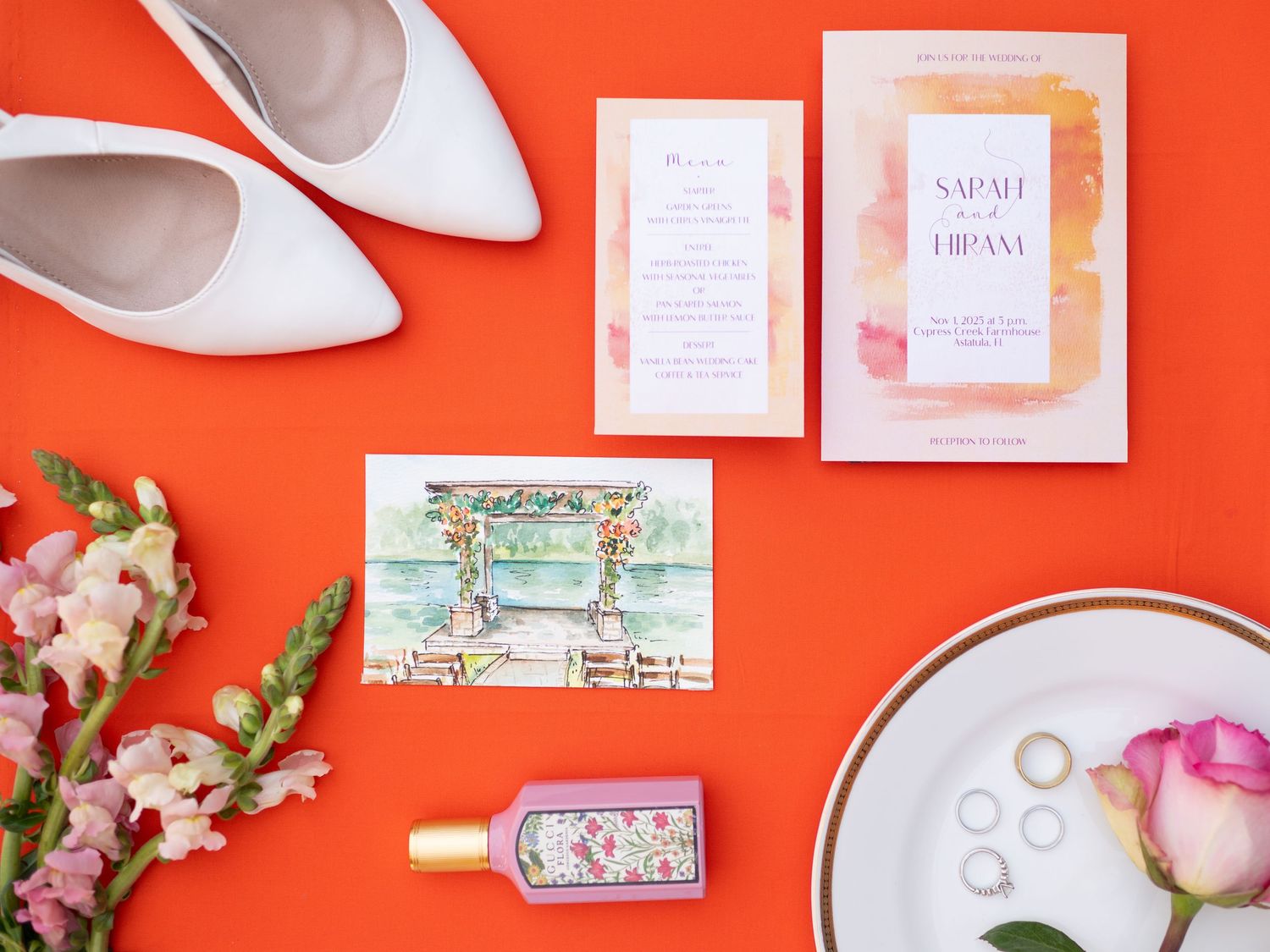 Wedding accessories and invitations arranged on vibrant coral red background.