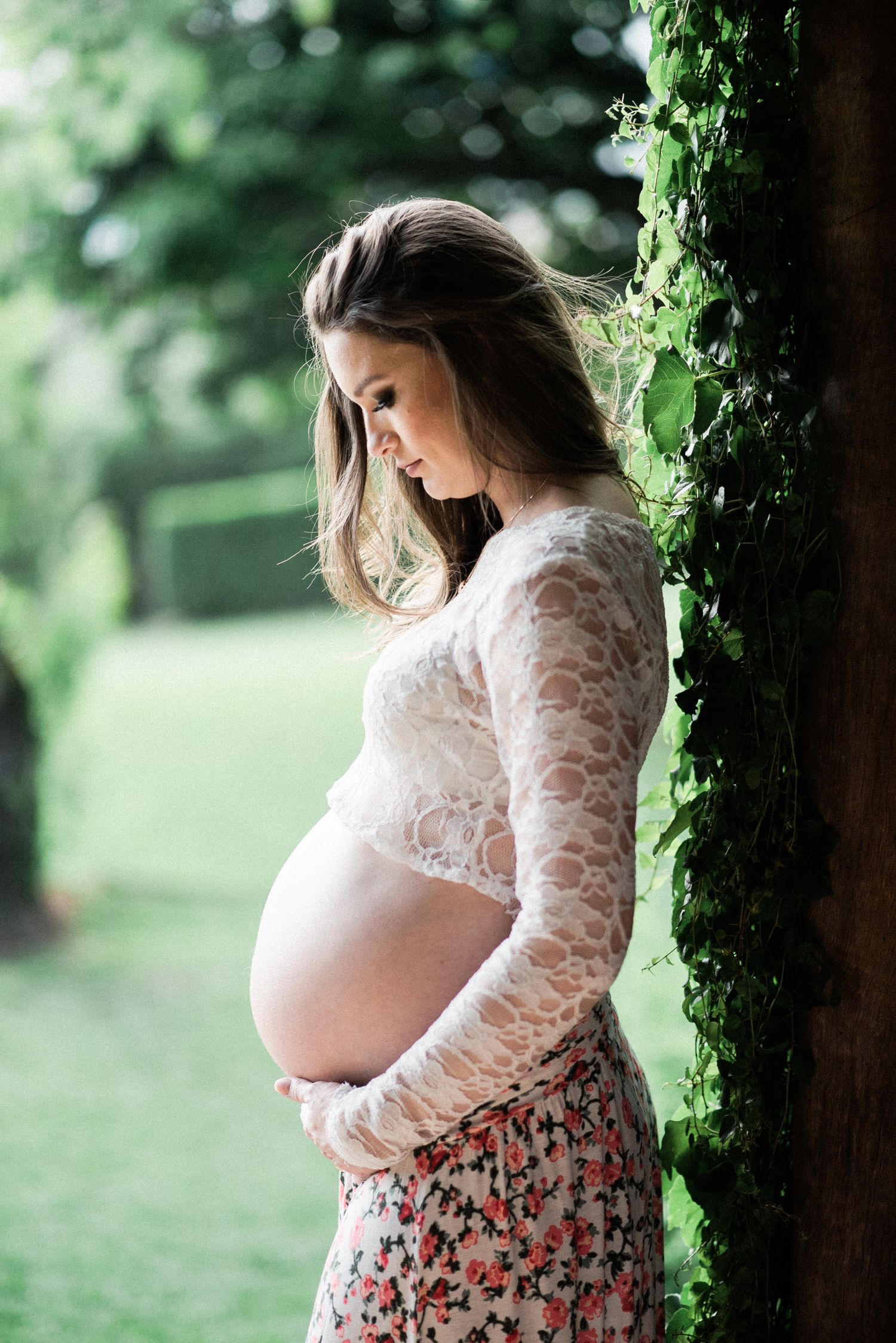 Maternity photos show woman in lace top against mossy trees in outdoor setting.