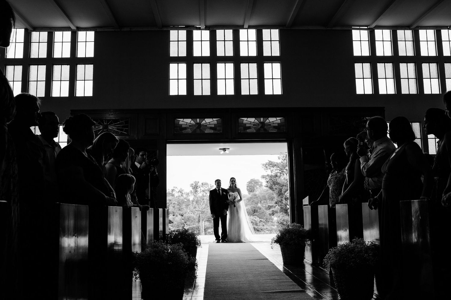 Dramatic silhouettes of wedding guests in a venue with large windows.