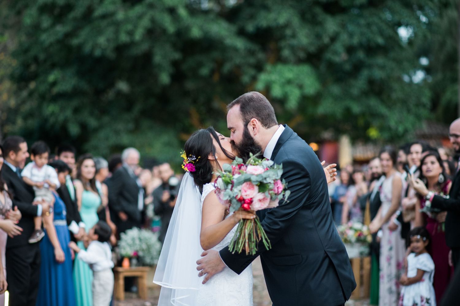 Wedding celebration with guests outdoors surrounded by lush greenery.