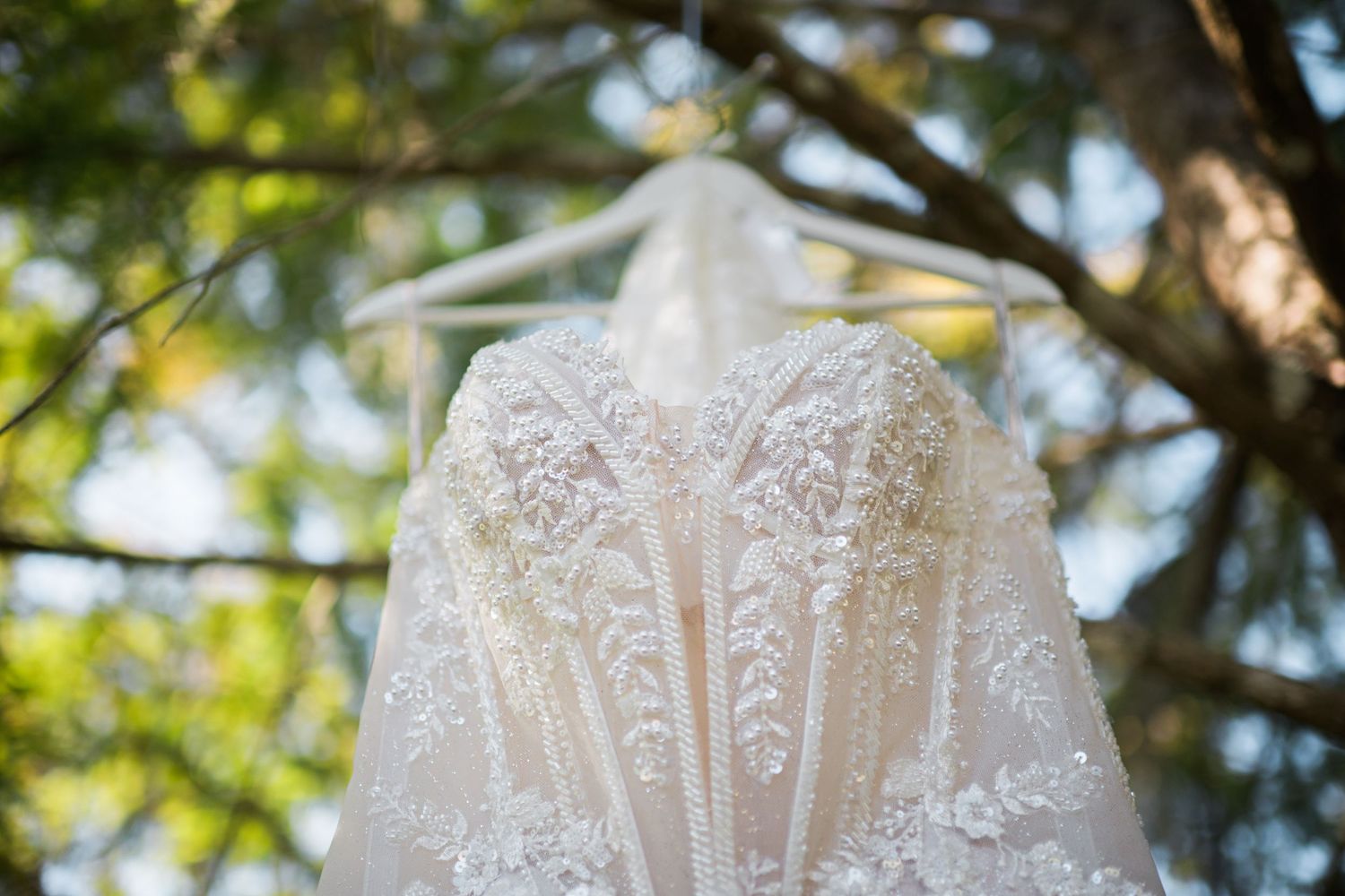 Delicate lace patterns and beading details of a wedding gown in natural light.