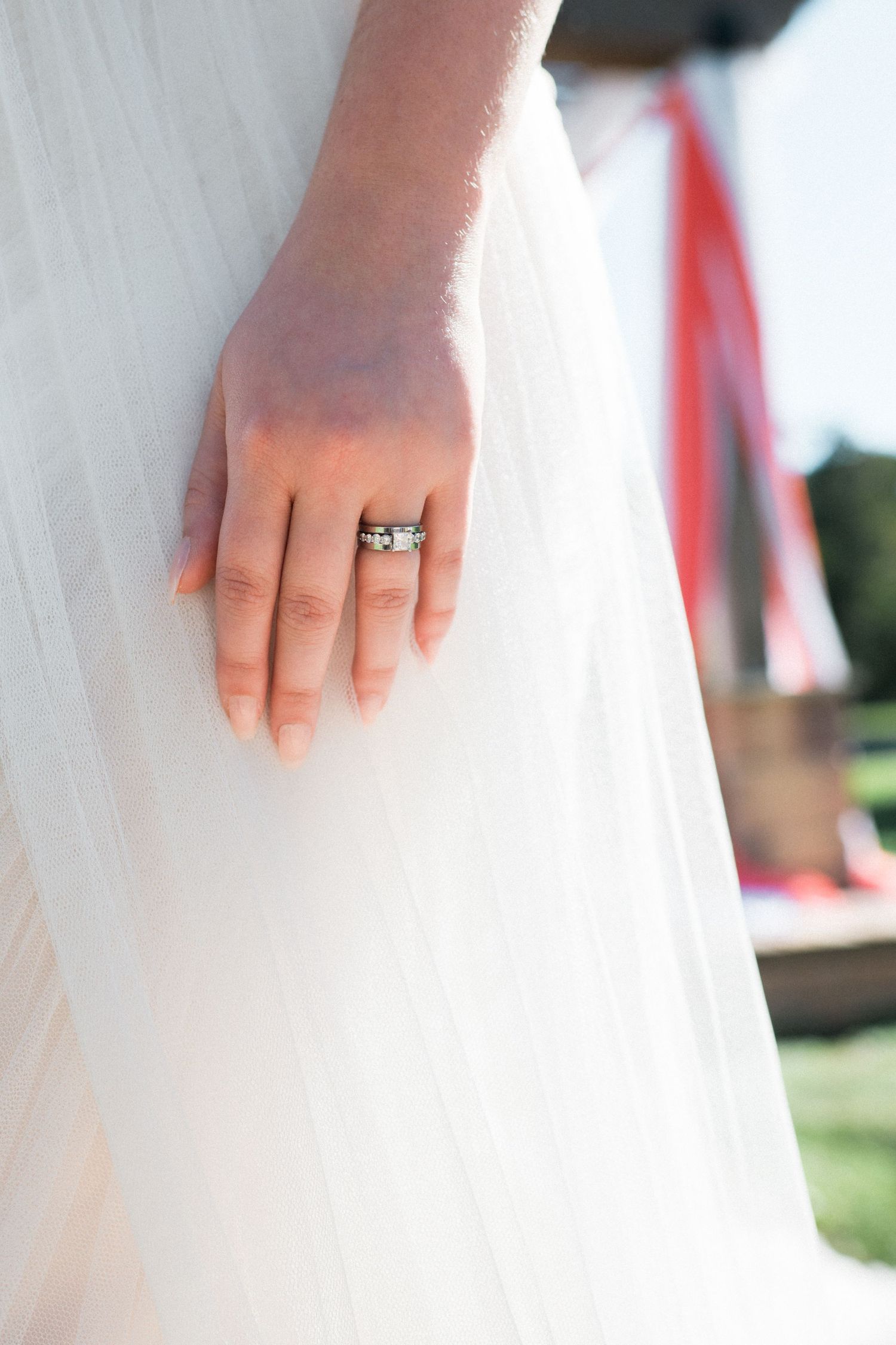 Close-up of a wedding ring on a hand against a white dress.