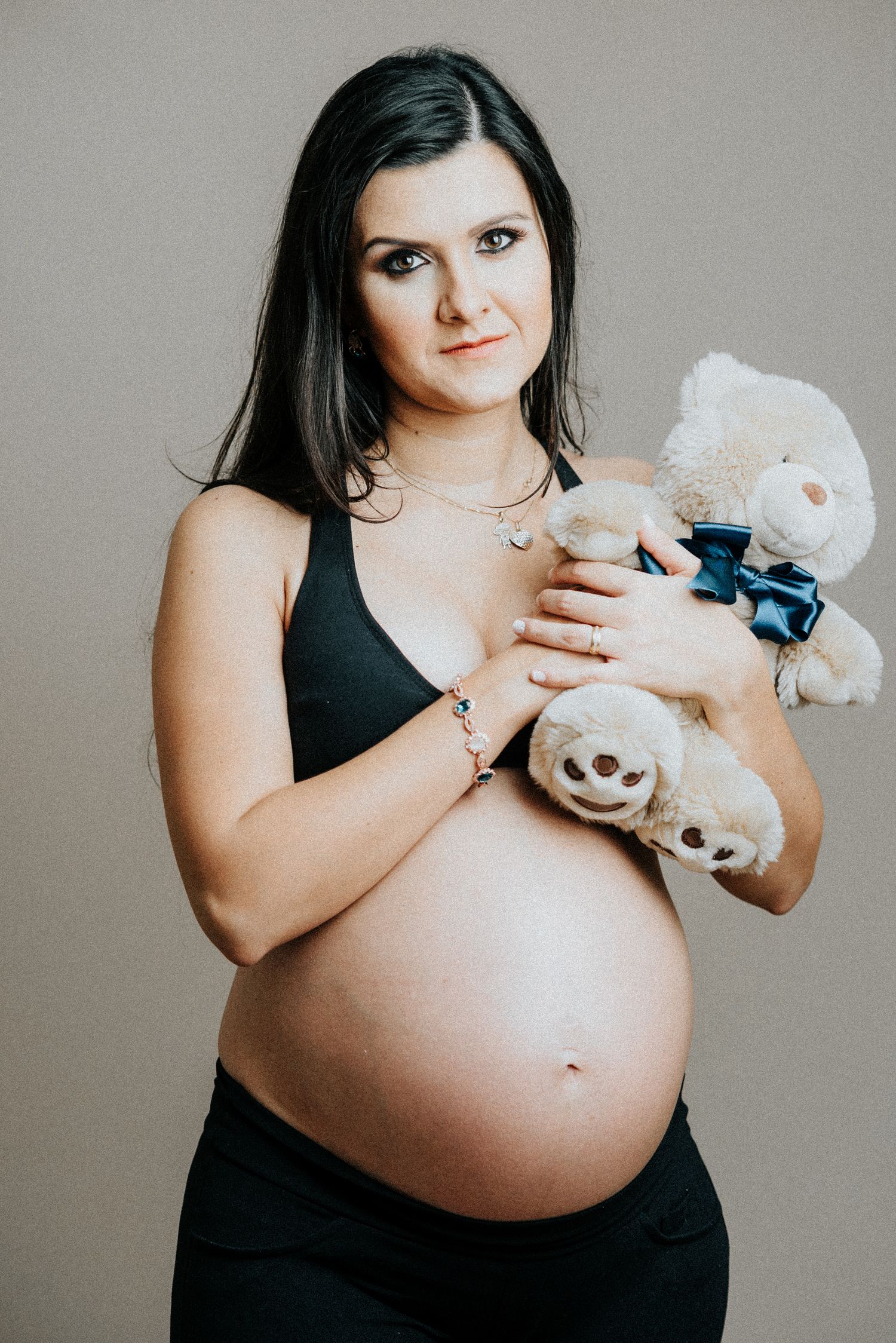 Expecting mother in black holding white stuffed animals against her pregnant belly in progression.