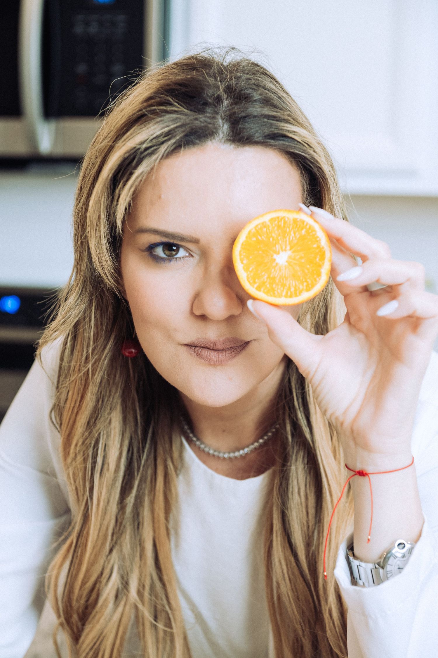 Playful portraits holding an orange slice in front of face while wearing a white top.