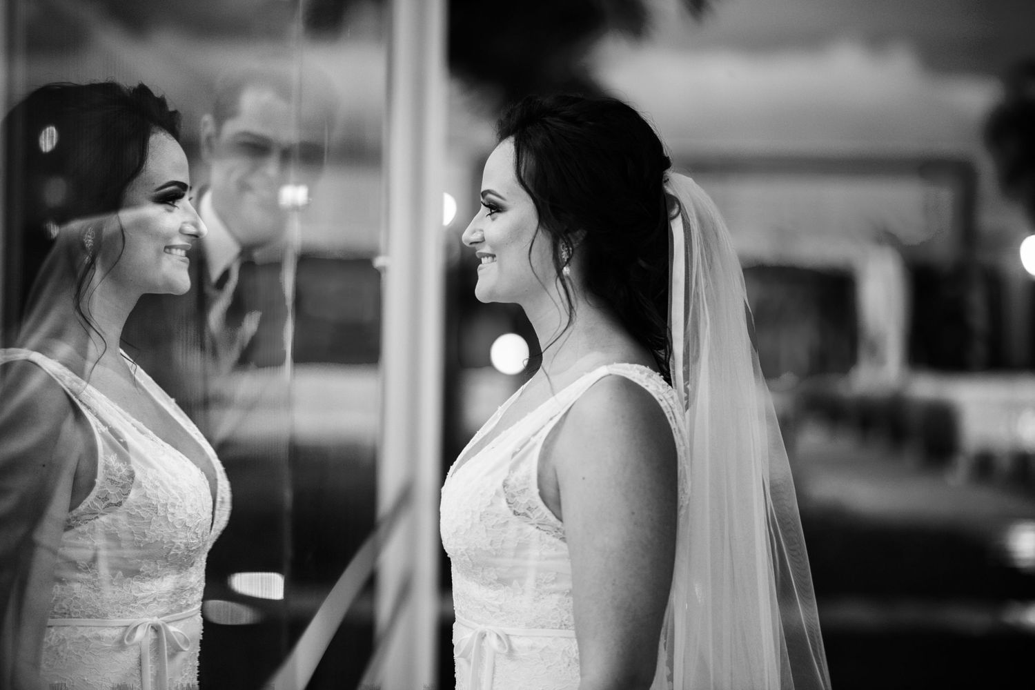 Black and white portrait of a bride in soft window light wearing delicate veil.
