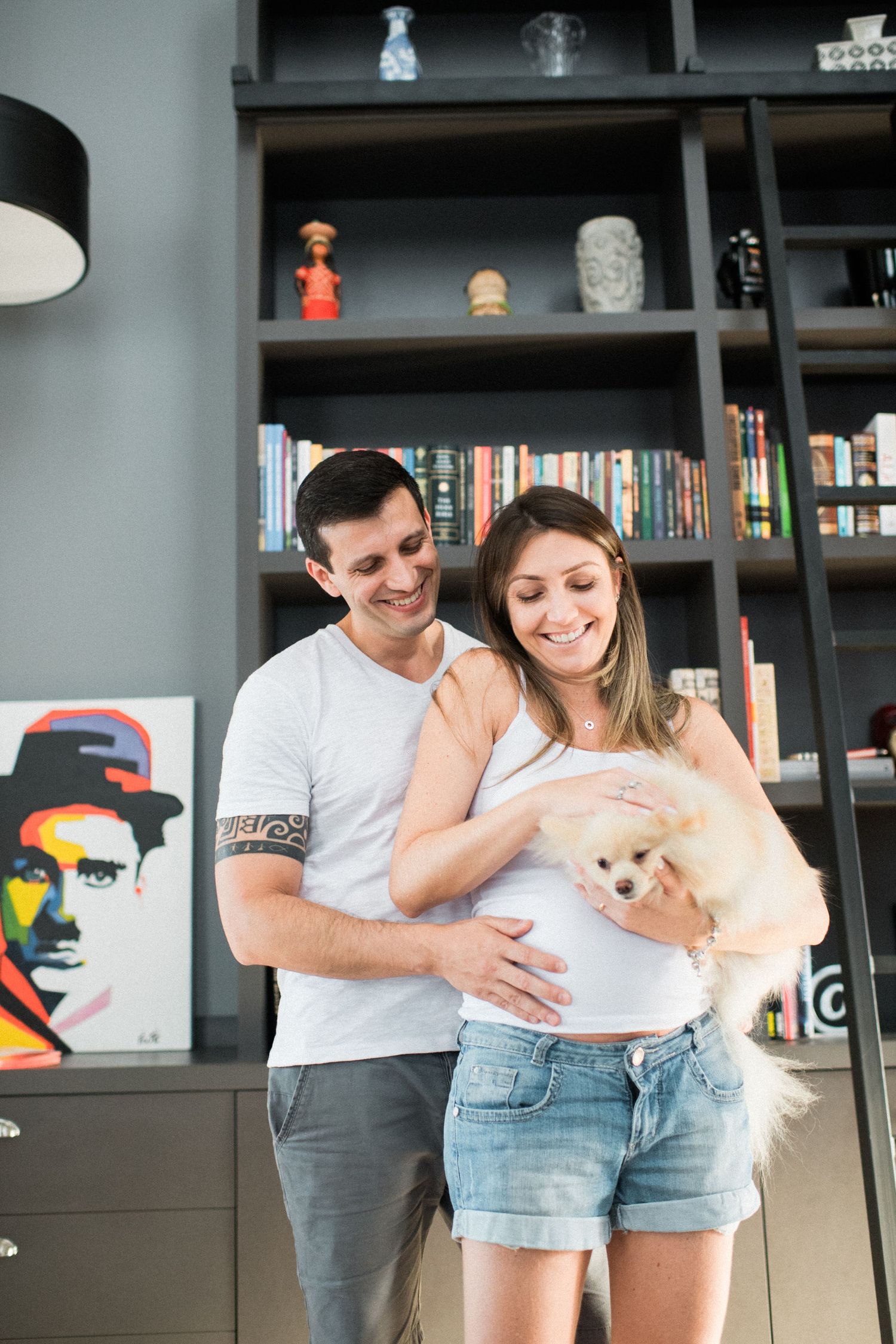 Happy couple embracing in their home library with a small cream-colored dog.